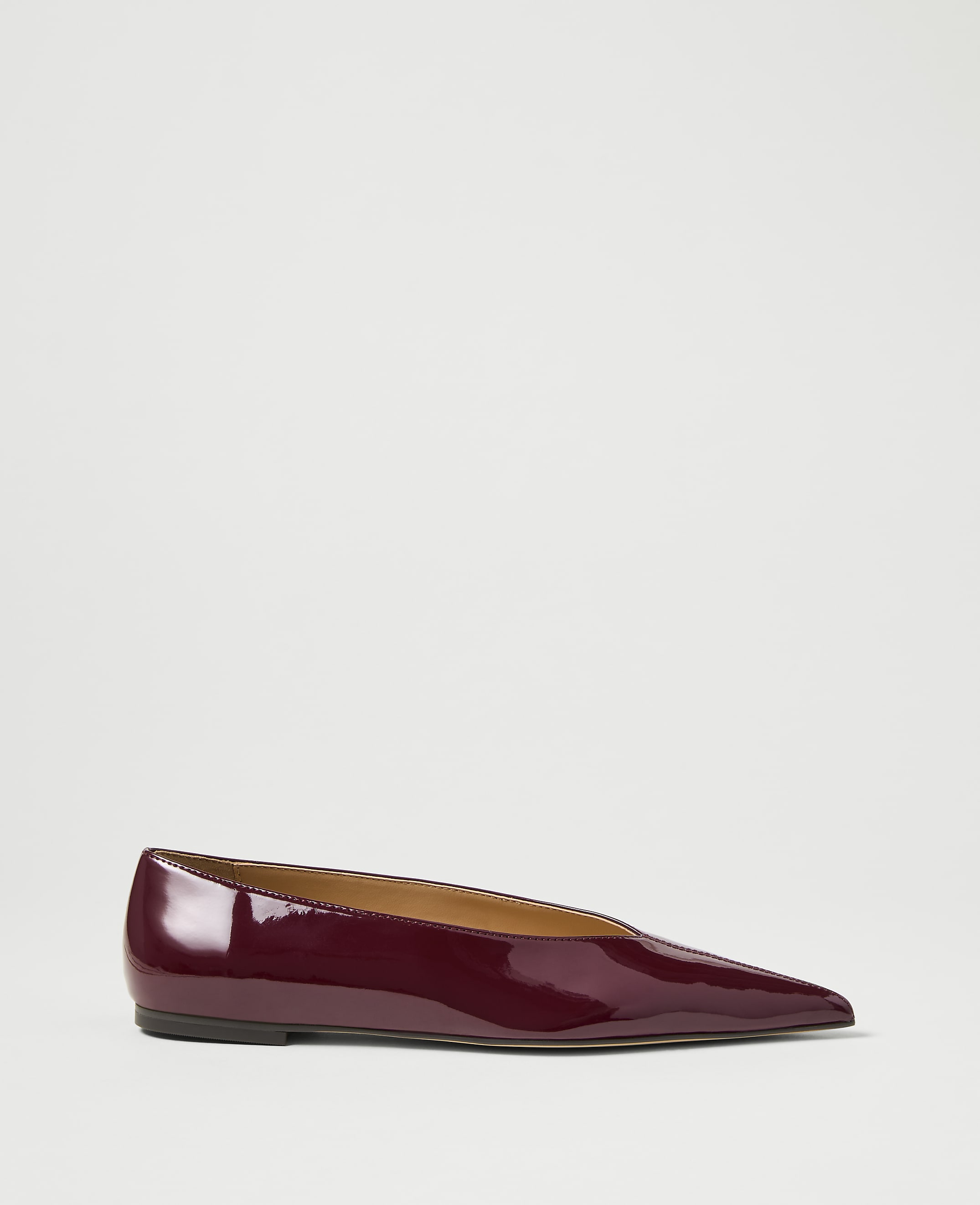 A glossy burgundy pointed-toe flat shoe rests on a plain white background.