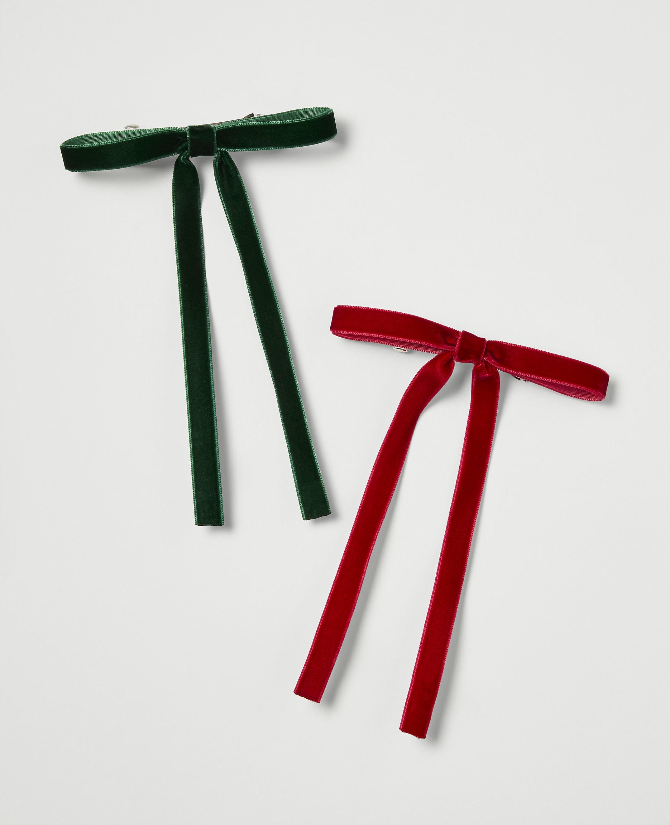 Two velvet bow ties, one green and one red, lie on a plain white background.