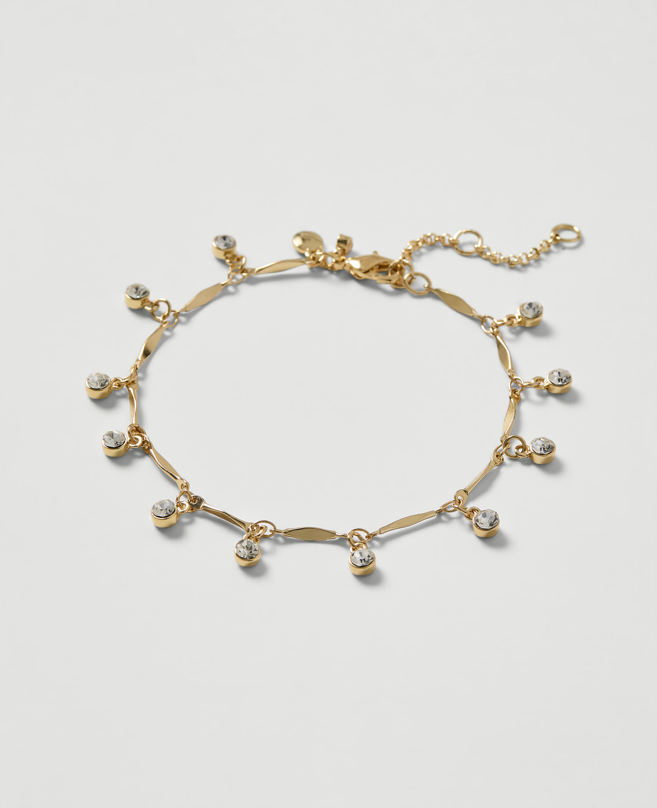A delicate gold bracelet with dangling clear crystals rests on a plain white background.