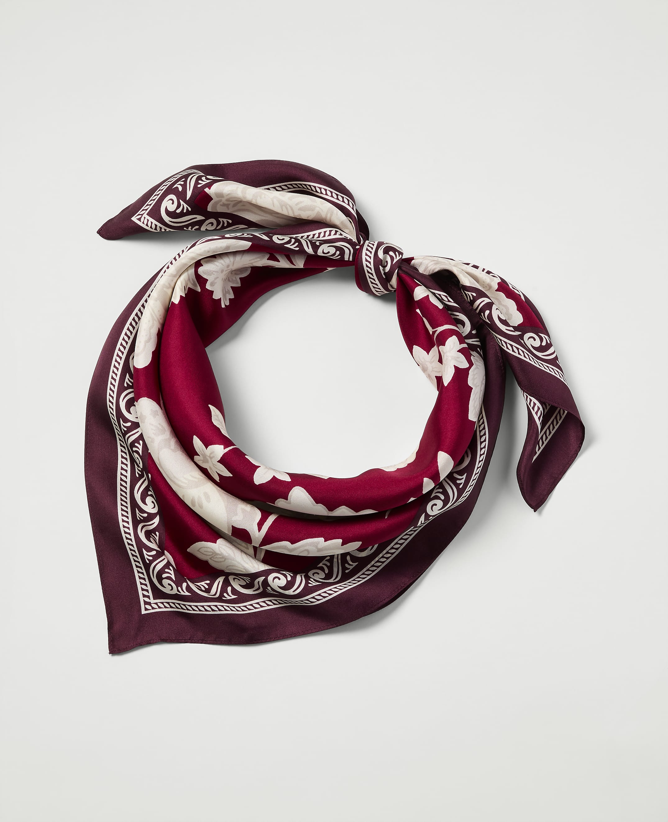 A burgundy and cream patterned silk scarf is tied in a knot against a plain white background.