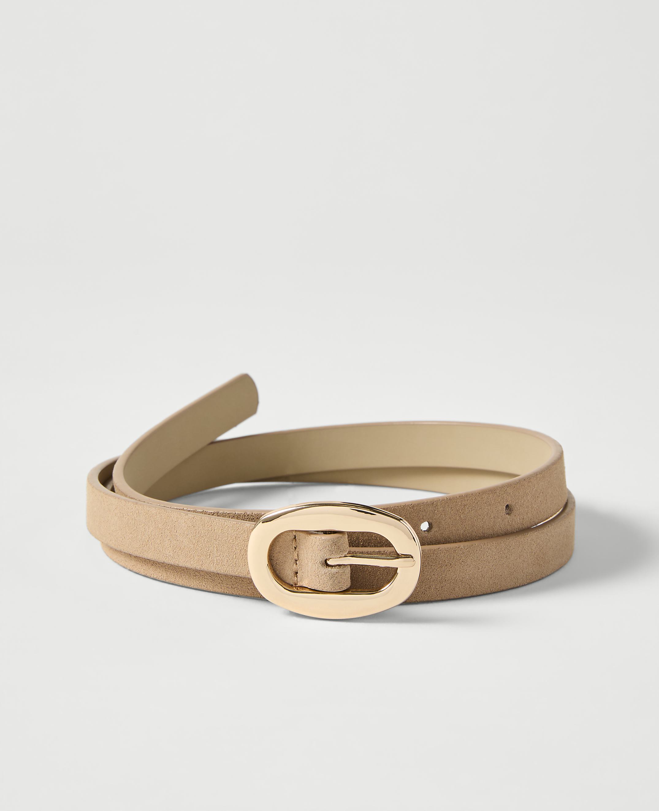 A tan suede belt with a gold oval buckle lies coiled on a plain white background.