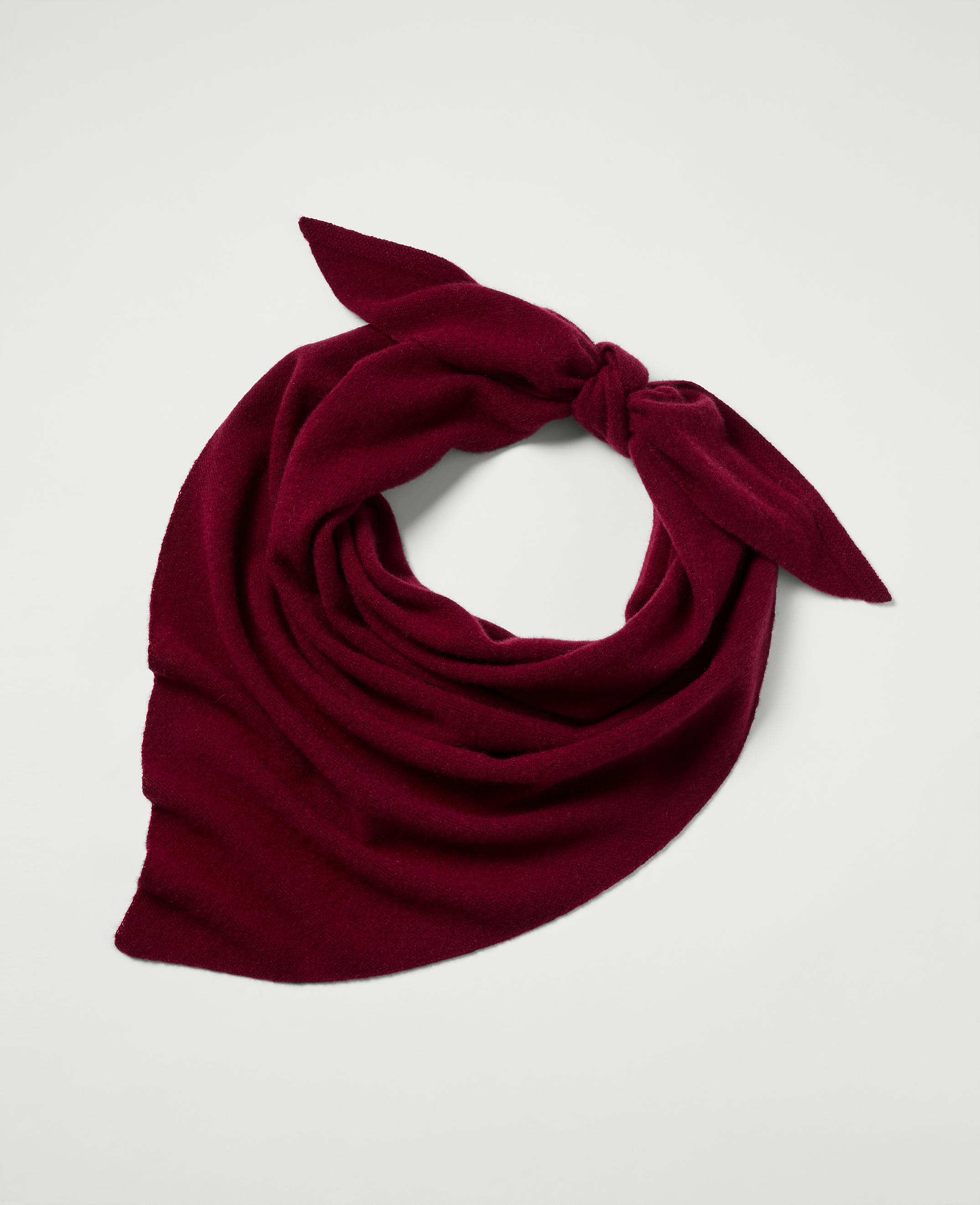 A deep red scarf is tied in a knot with its ends fanned out against a plain white background.
