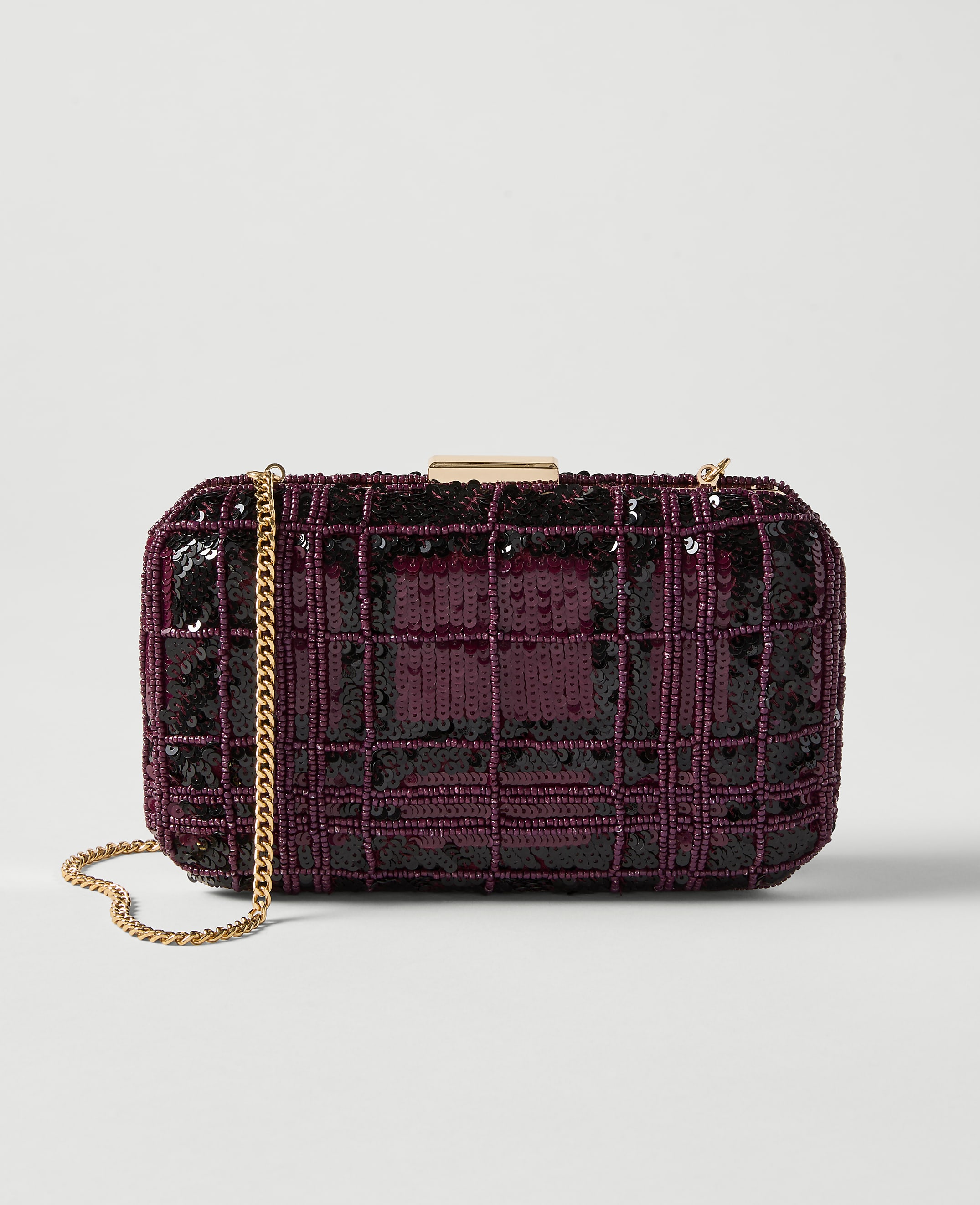 A rectangular, plum-colored sequined clutch with a gold chain strap rests on a plain white background.