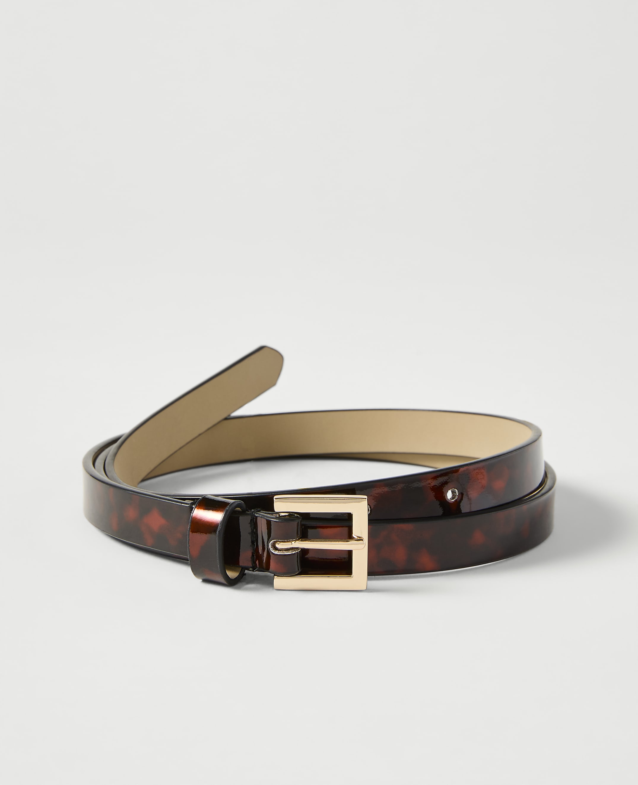 A thin, tortoiseshell-patterned belt with a gold buckle lies on a plain white background.