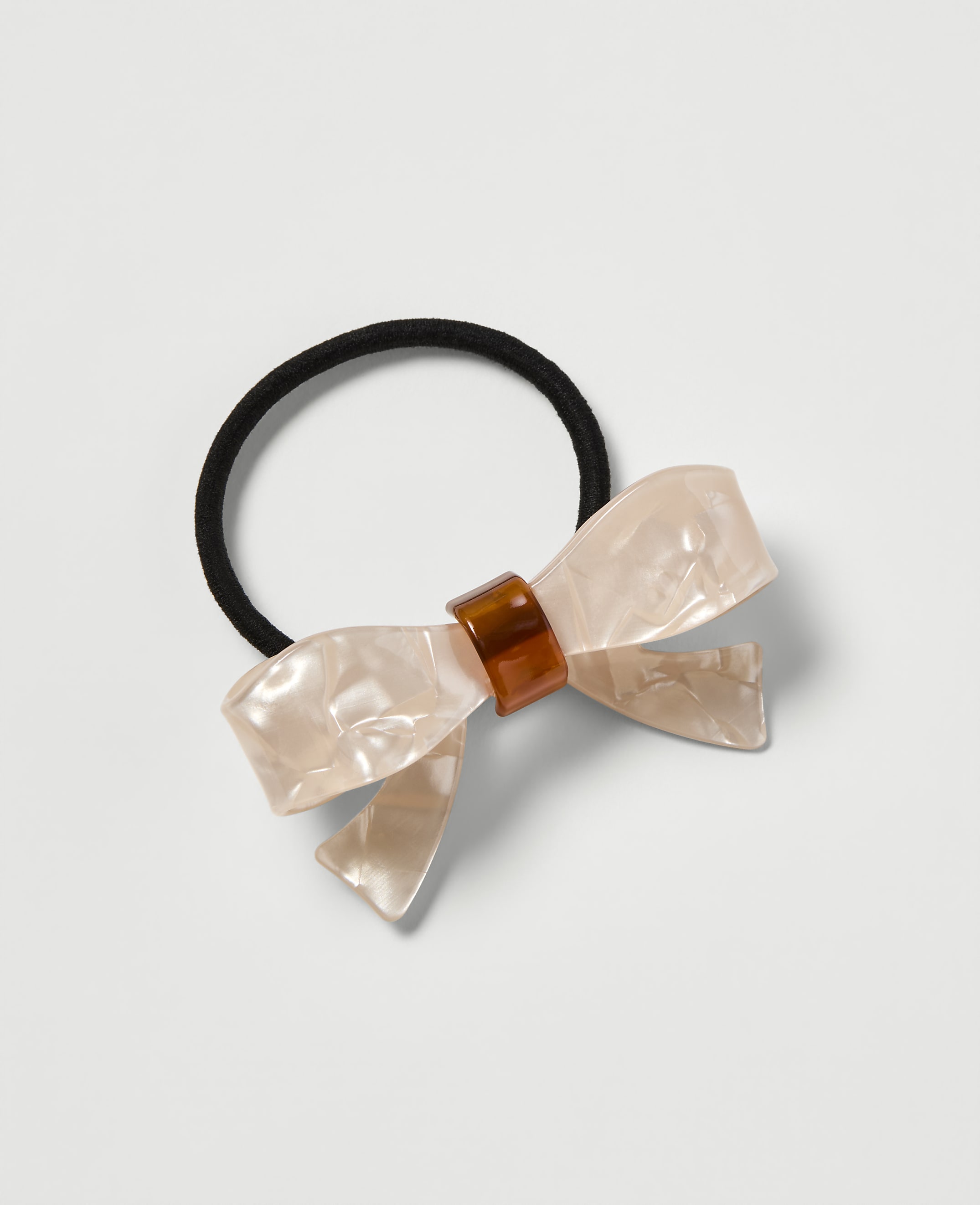 A pearlescent bow hair tie with a tortoiseshell accent rests on a plain white background.