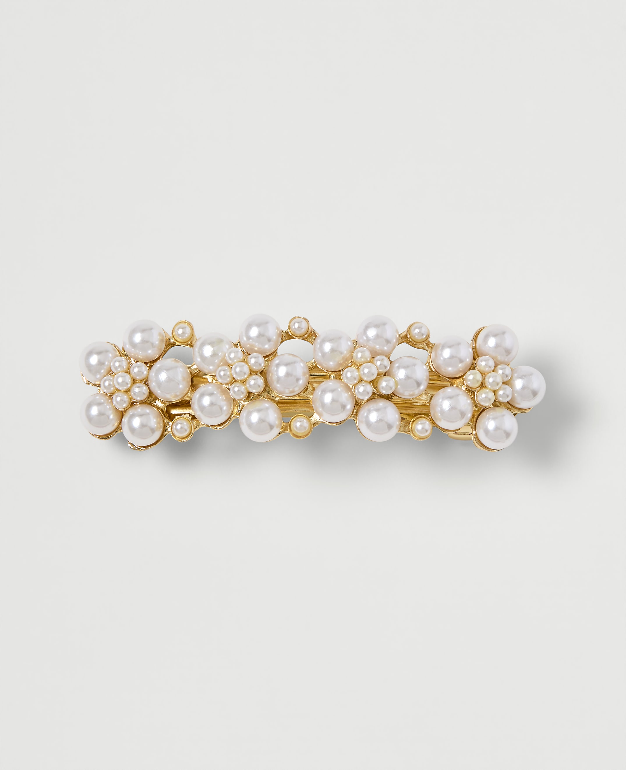 A gold barrette adorned with clusters of pearls sits on a plain, light-colored background.