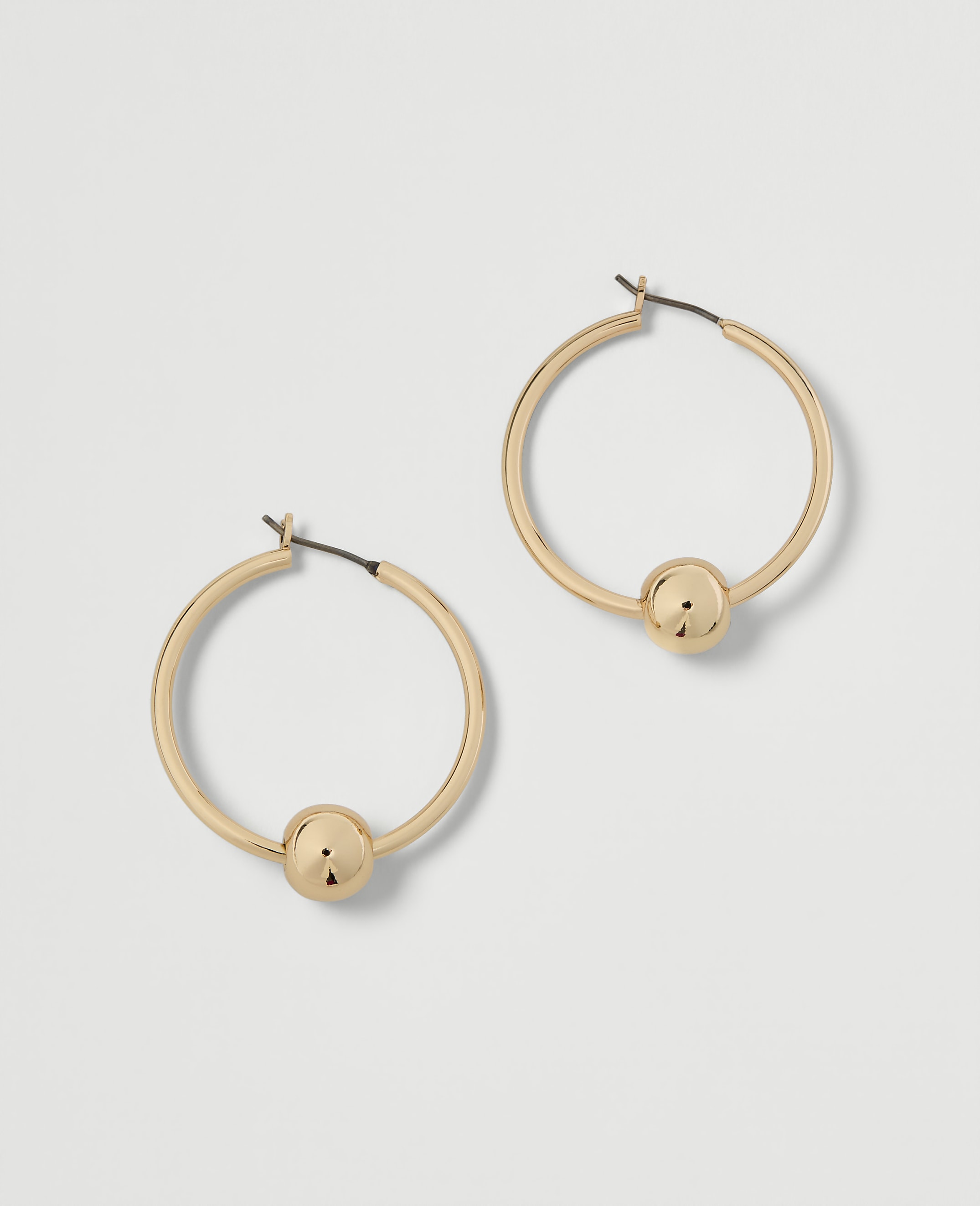 A pair of gold hoop earrings with a single bead on each rests on a plain white background.