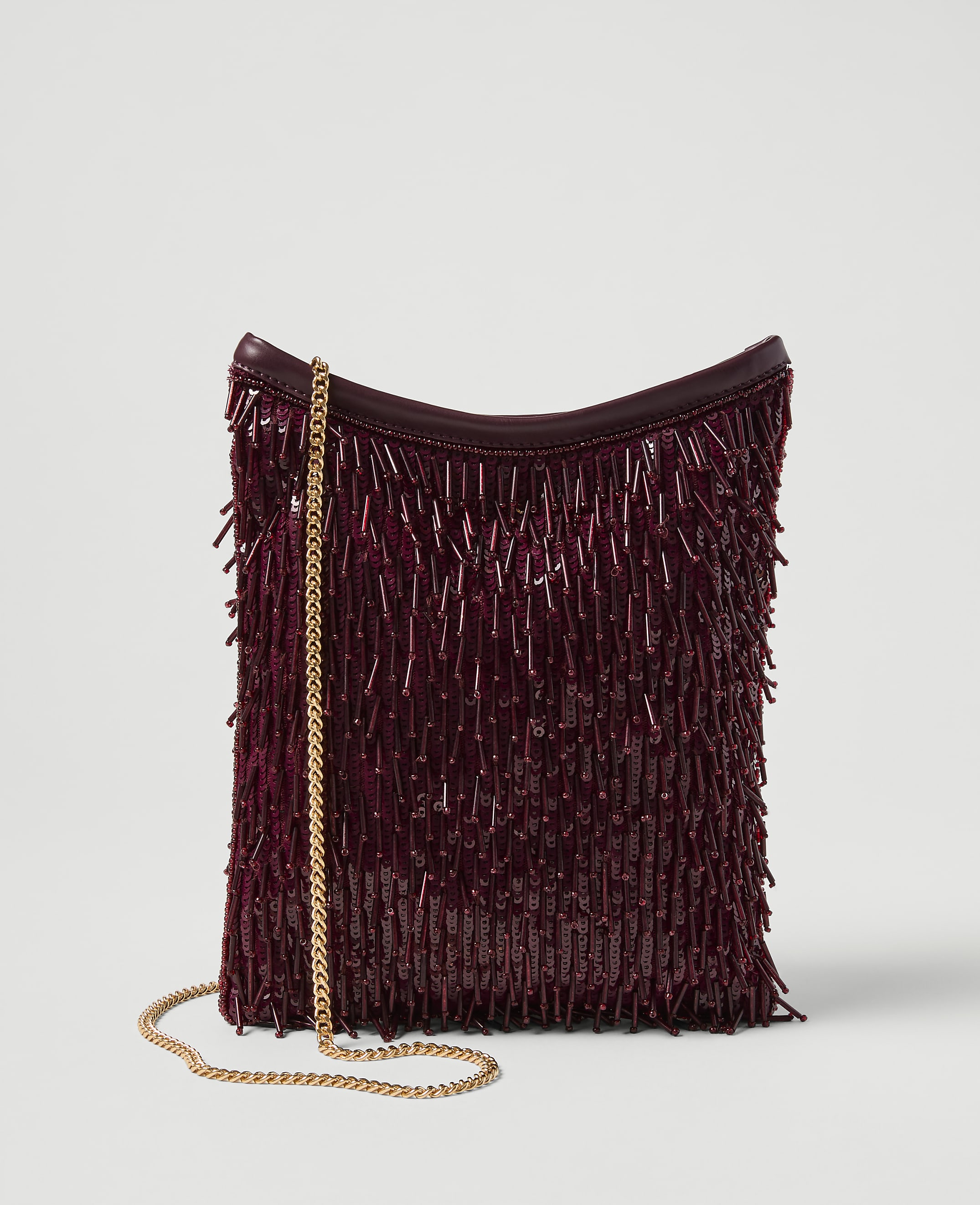 A burgundy beaded fringe clutch with a gold chain strap rests against a plain white background.