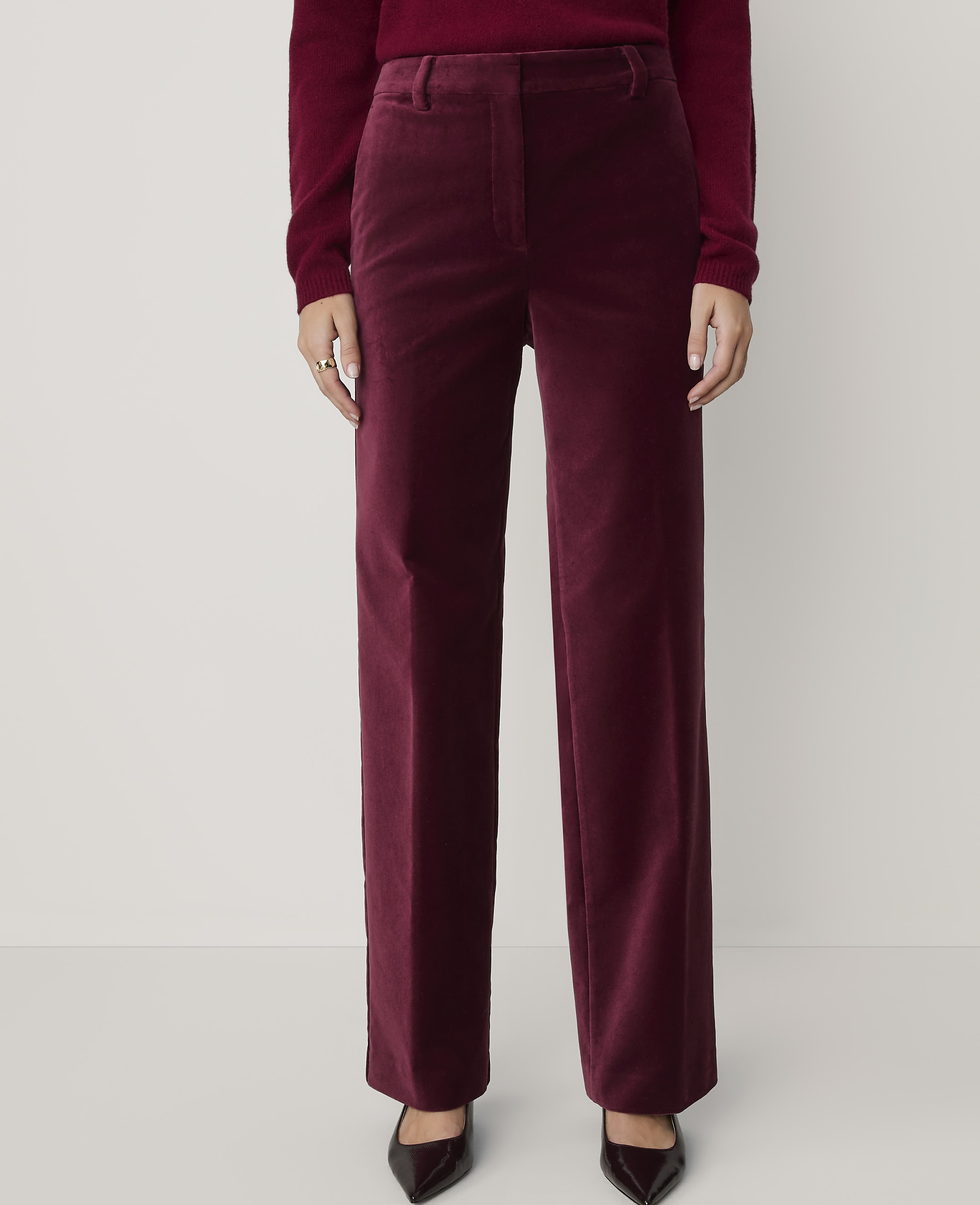 A person wearing burgundy velvet wide-leg pants and a matching sweater stands against a plain white background.