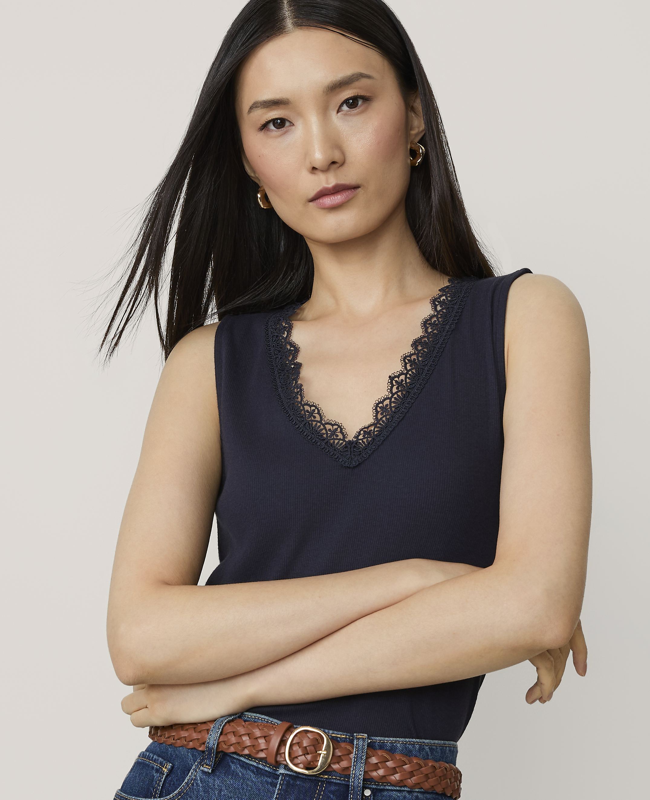 A woman in a navy blue tank top with lace trim poses with her arms crossed against a plain white background.