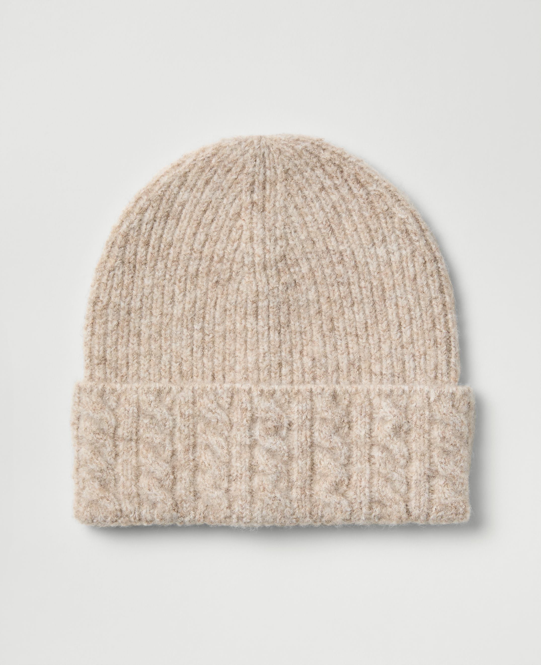 A light beige cable-knit beanie sits centered against a plain, light gray background.
