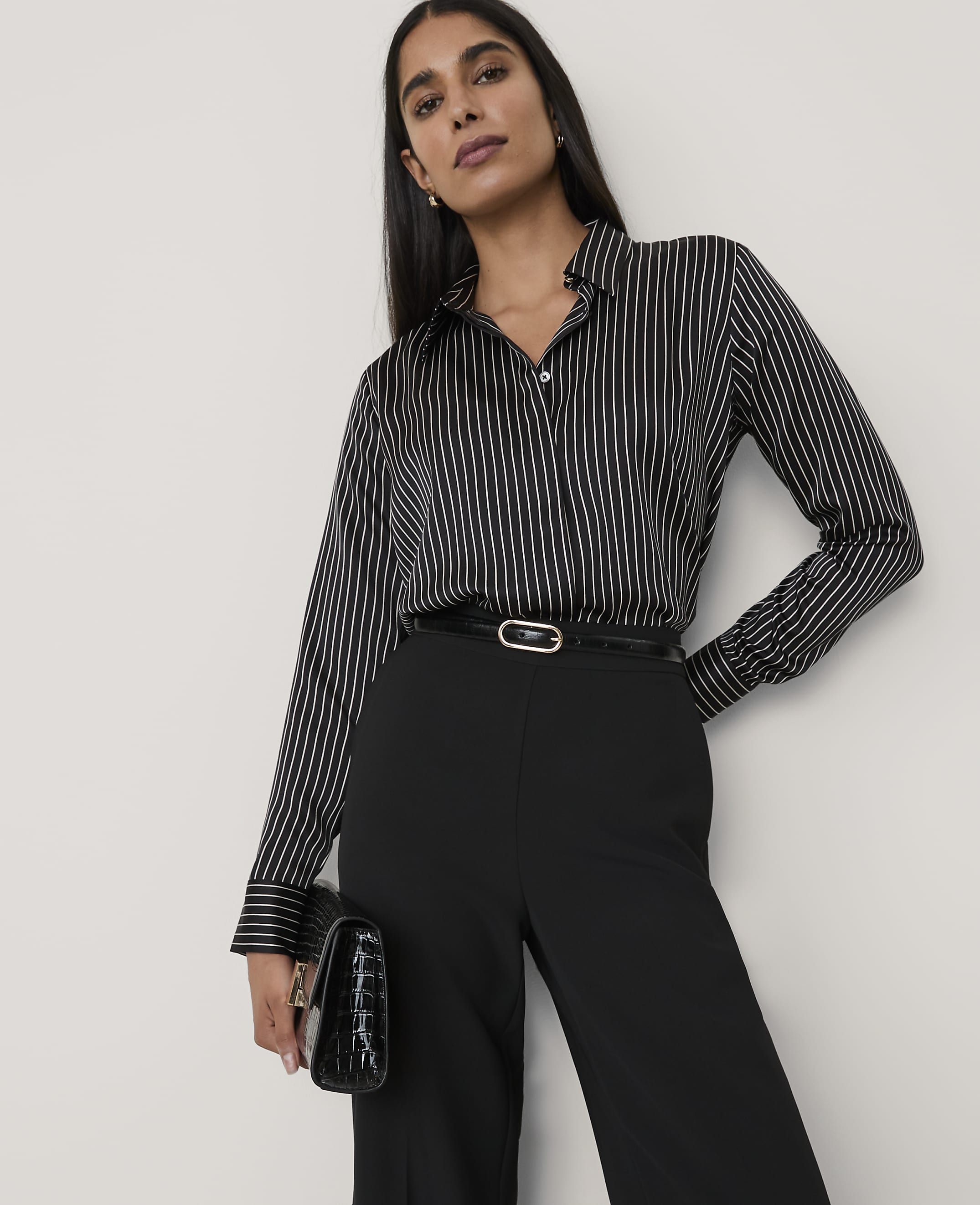 A woman wearing a black and white striped shirt and black trousers stands against a plain white background.
