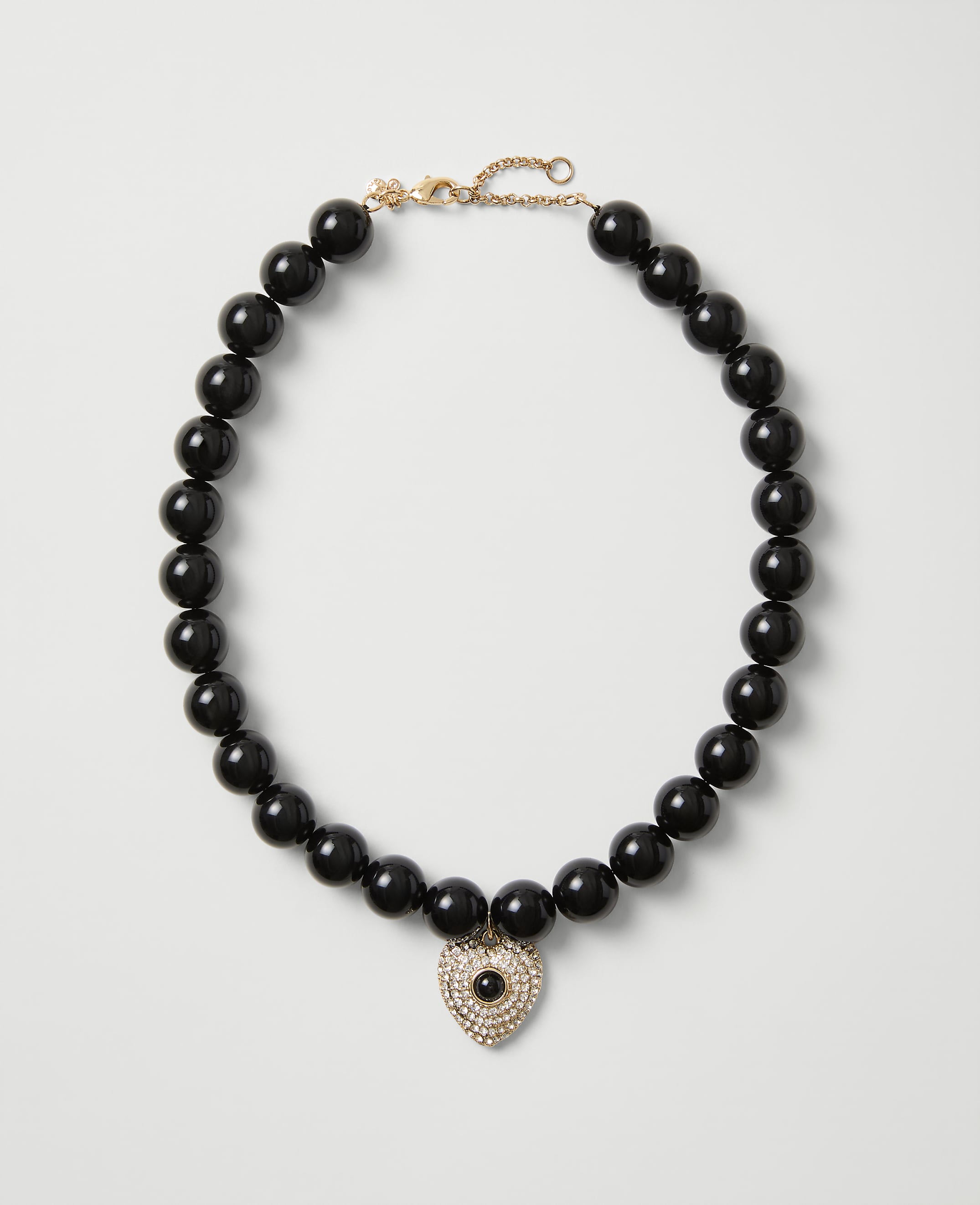 A necklace of polished black beads with a heart-shaped crystal pendant rests on a plain light gray background.