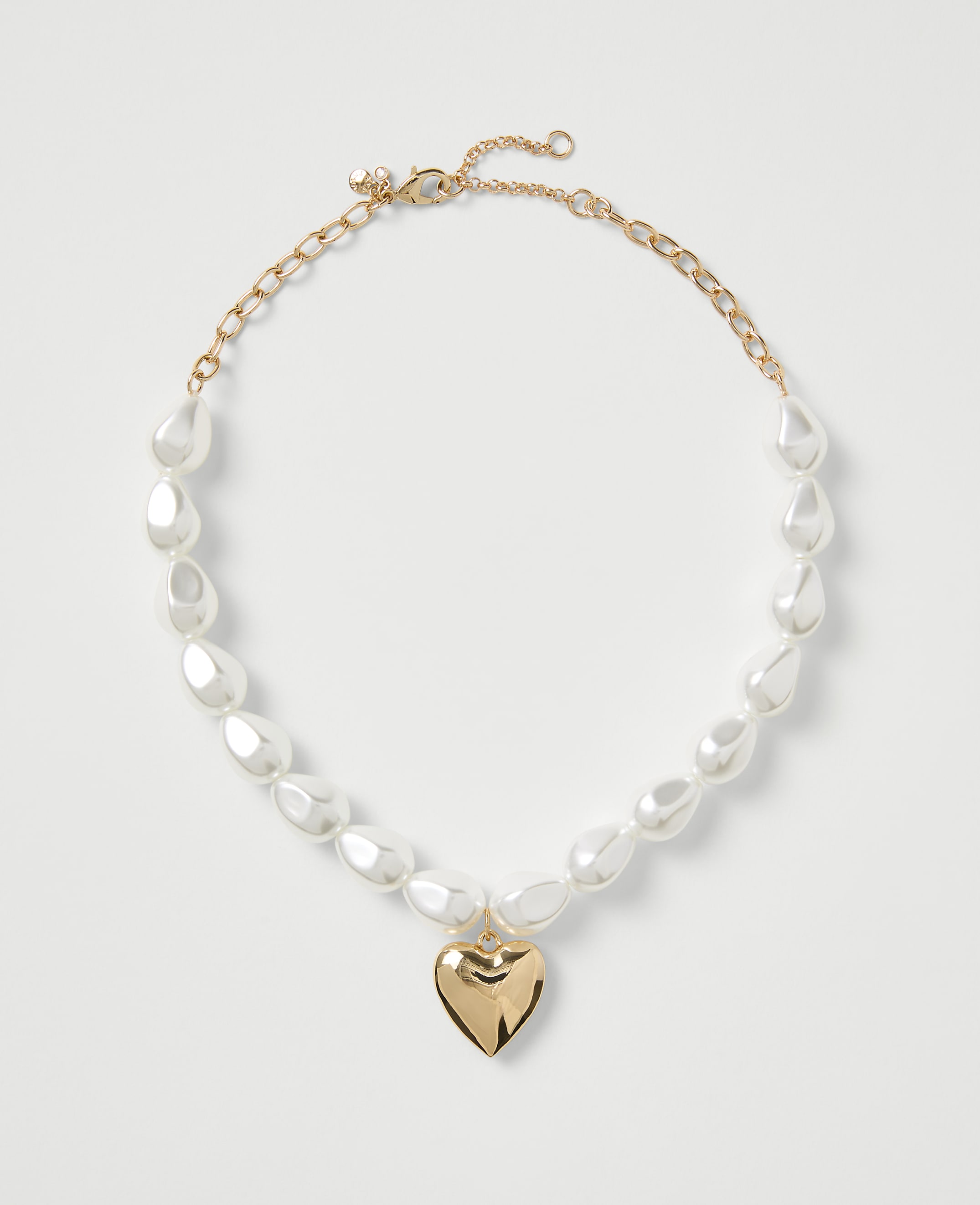 A gold-toned necklace with white teardrop pearls and a heart pendant rests on a plain white background.