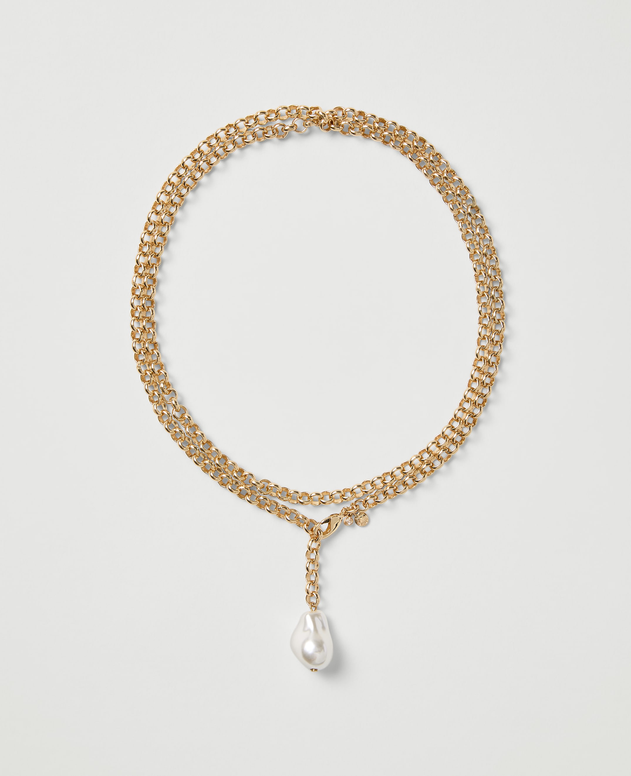A gold chain necklace with a single white pearl drop pendant rests on a plain light gray background.