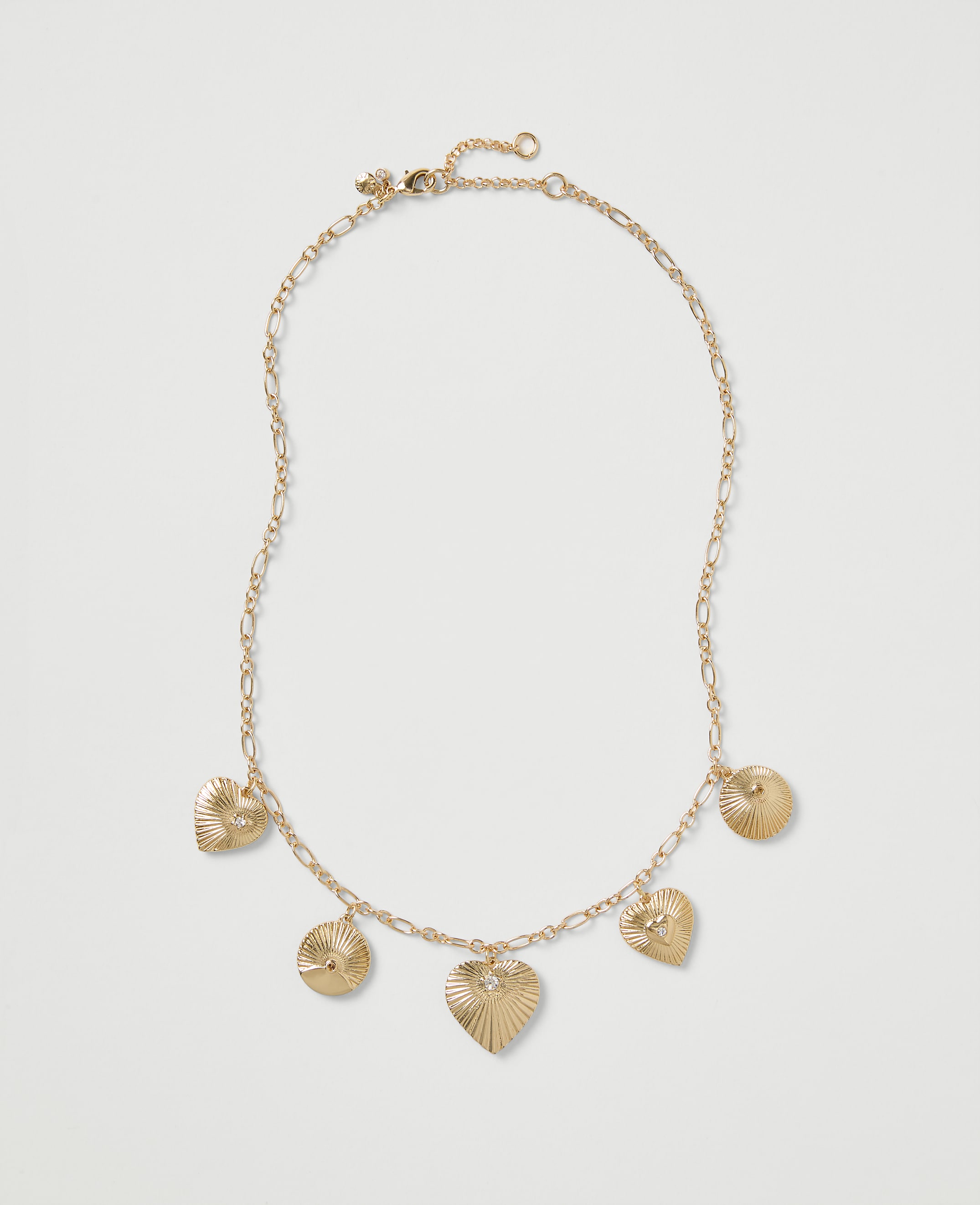 A gold chain necklace with heart and circular ribbed charms rests on a plain light gray background.