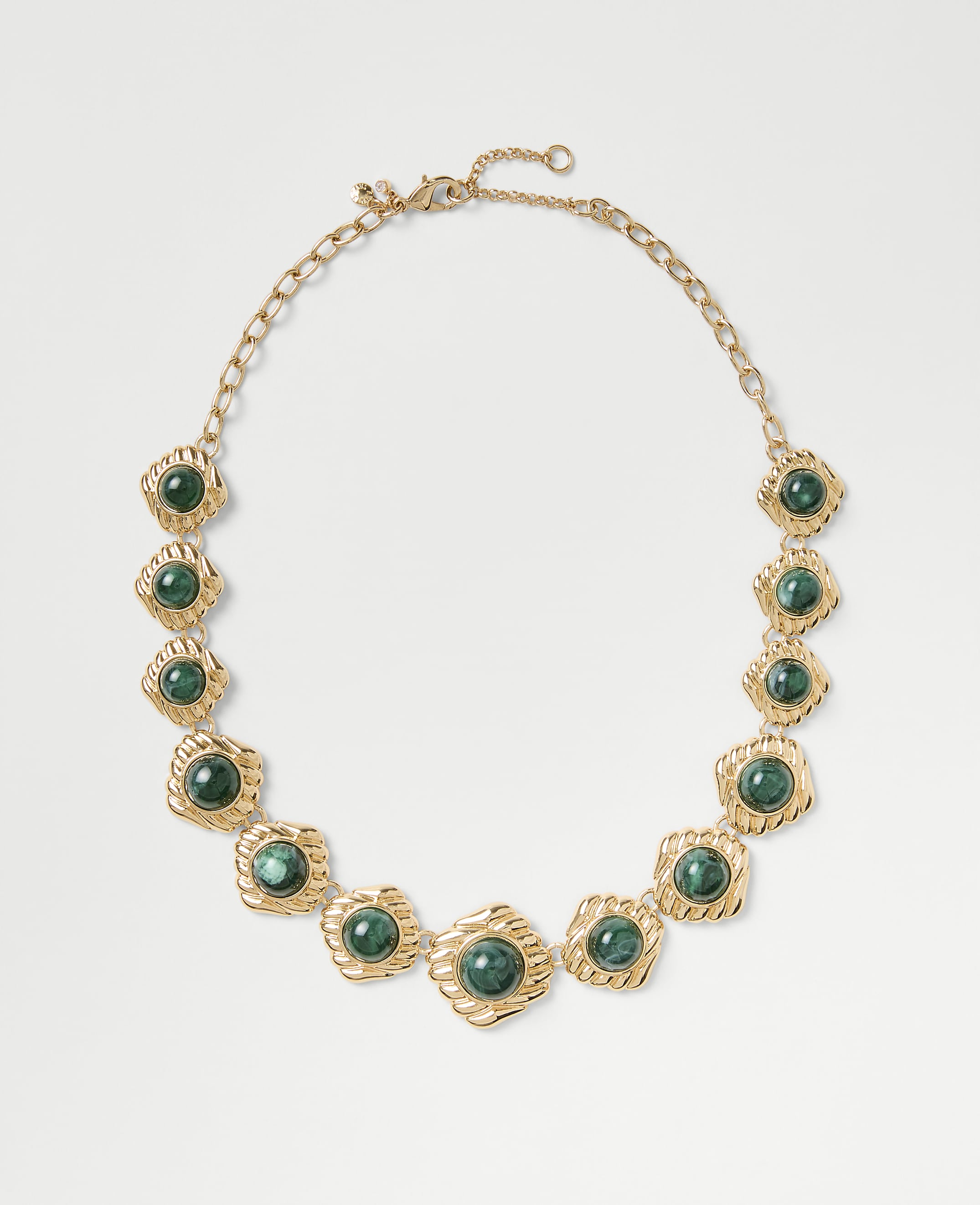 A gold chain necklace featuring green circular gemstones is centered against a plain light gray background.