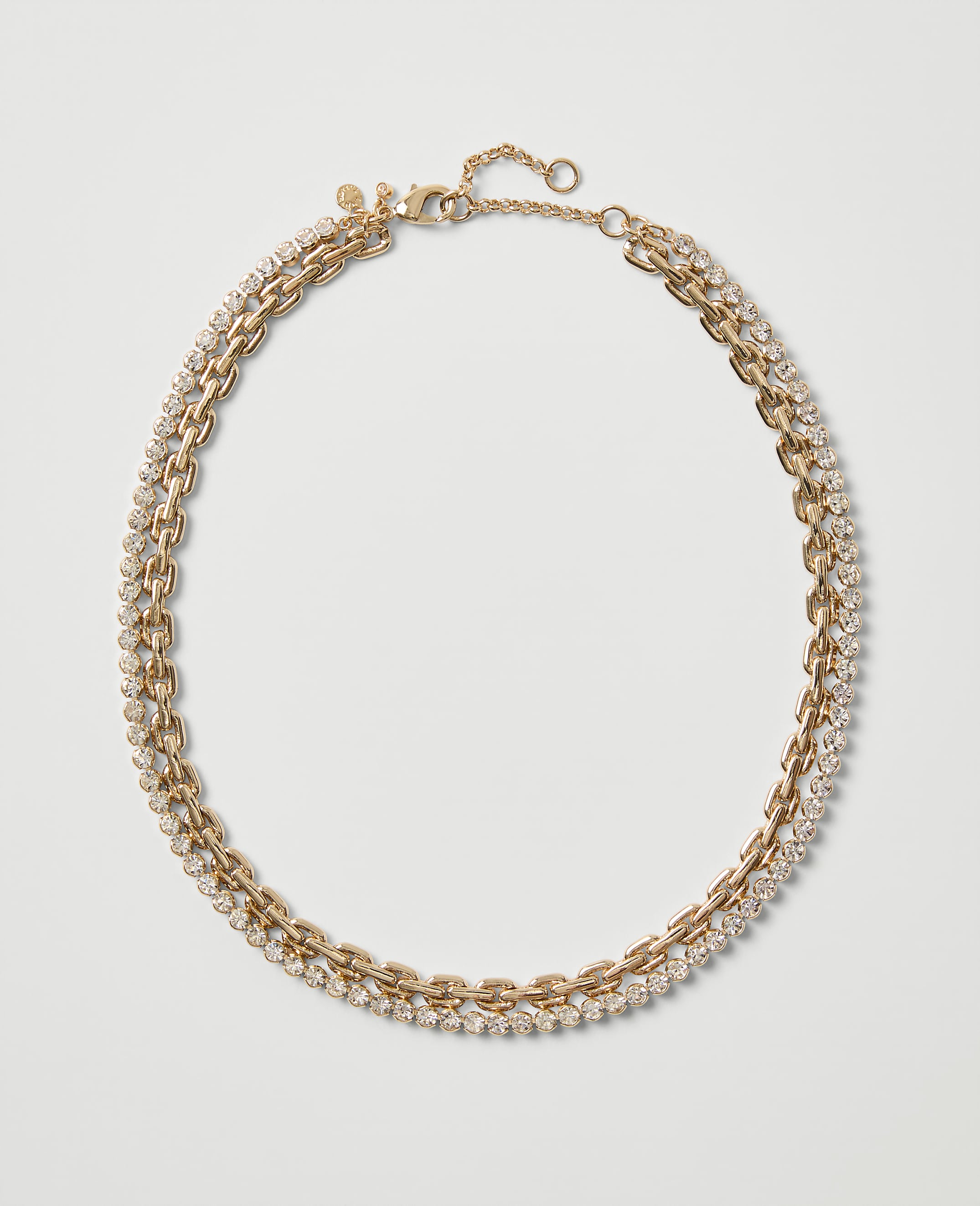 A gold-toned chain necklace embellished with sparkling crystals rests on a plain, light gray background.