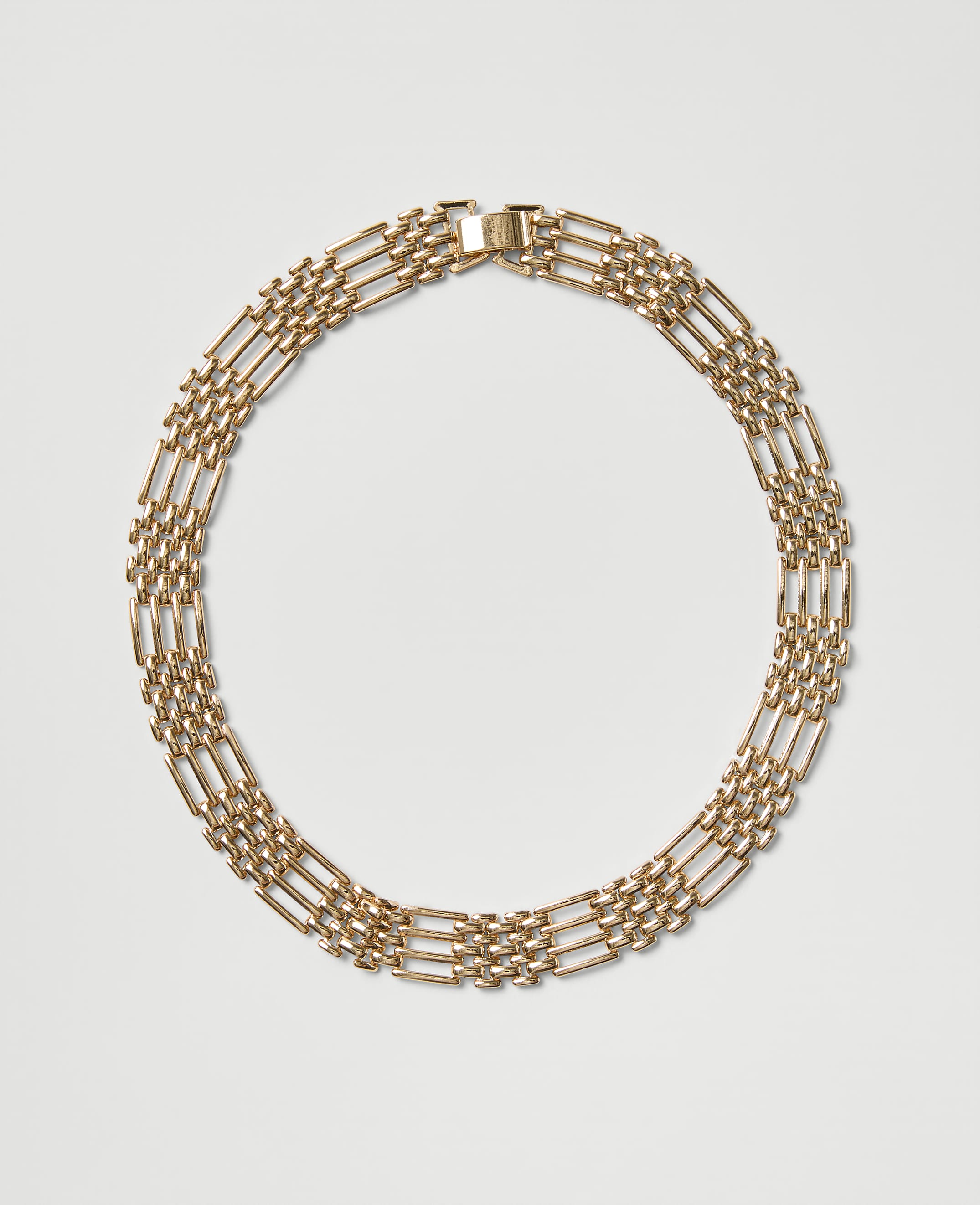 A gold chain necklace is arranged in a circle against a plain light gray background.