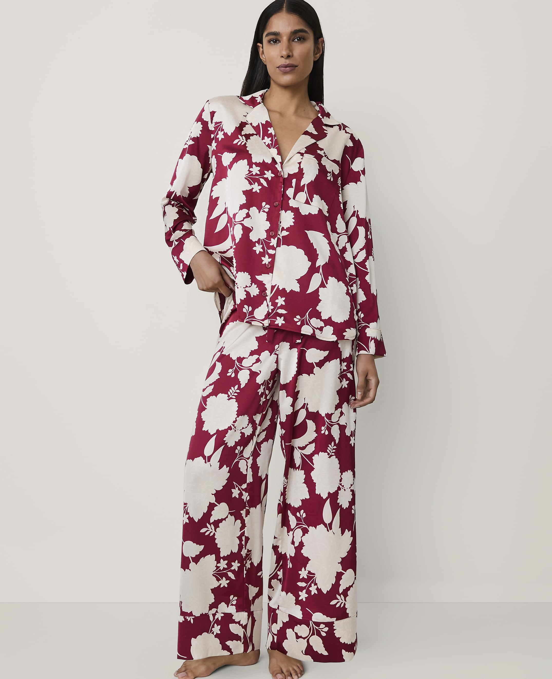 A woman wearing red and white floral pajamas stands against a plain, light-colored background.