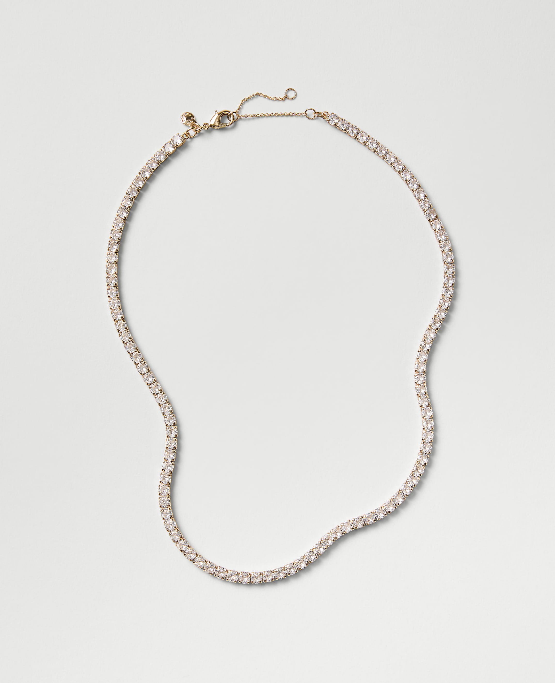 A sparkling tennis necklace with clear stones rests on a plain, light gray background.