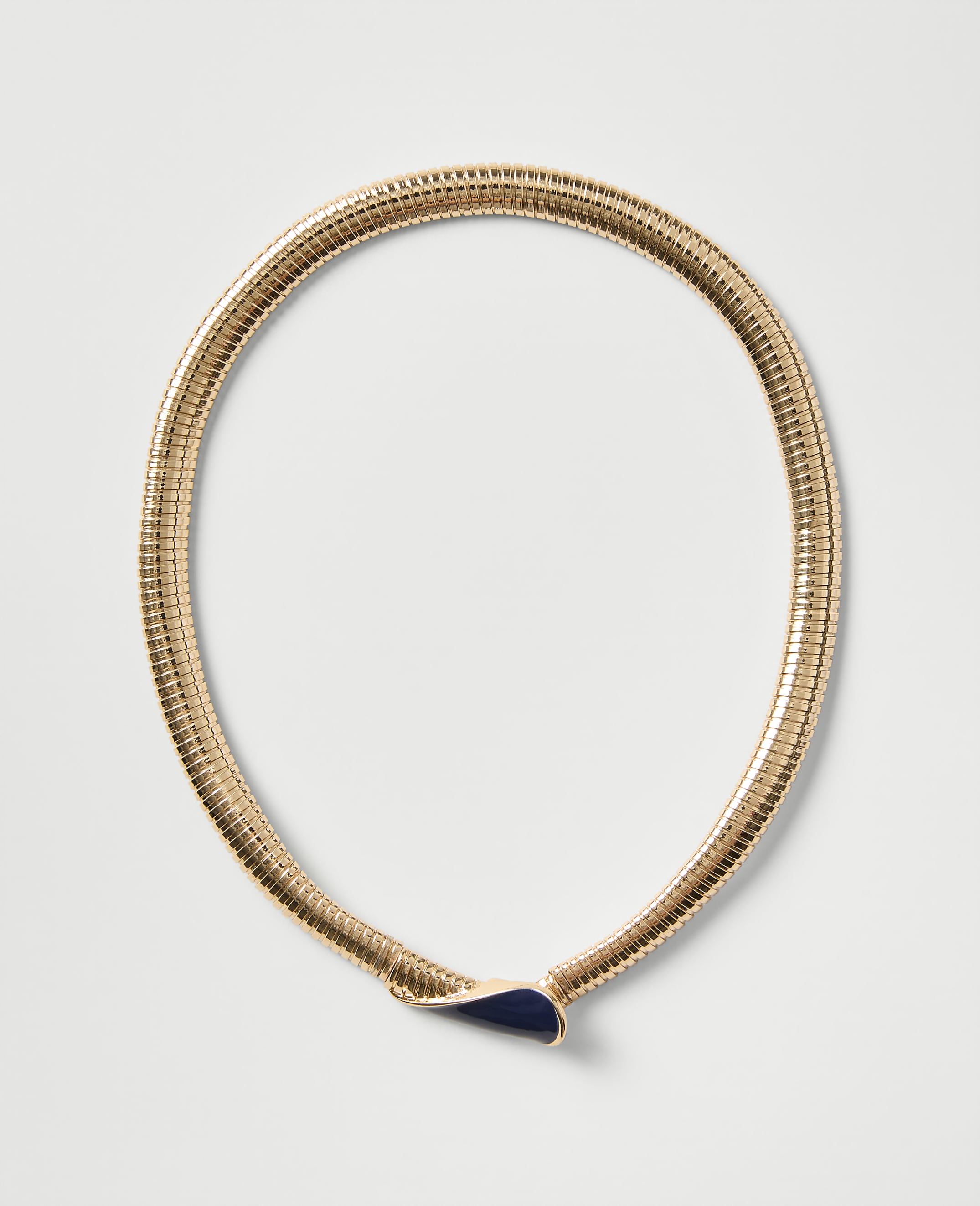 A gold ribbed necklace with a dark blue teardrop-shaped pendant rests on a plain light gray background.