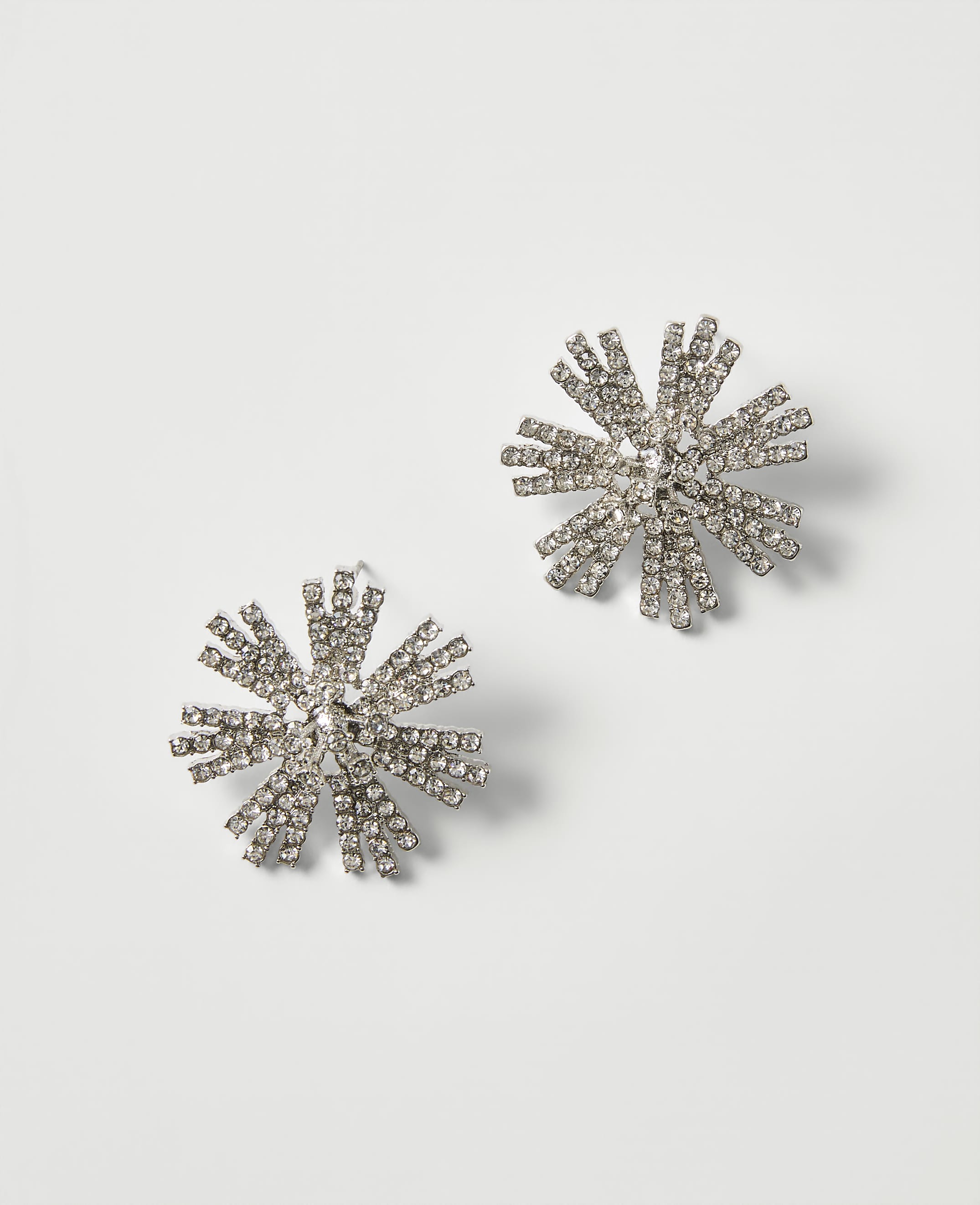 Two starburst-shaped crystal earrings rest on a plain, light gray background.