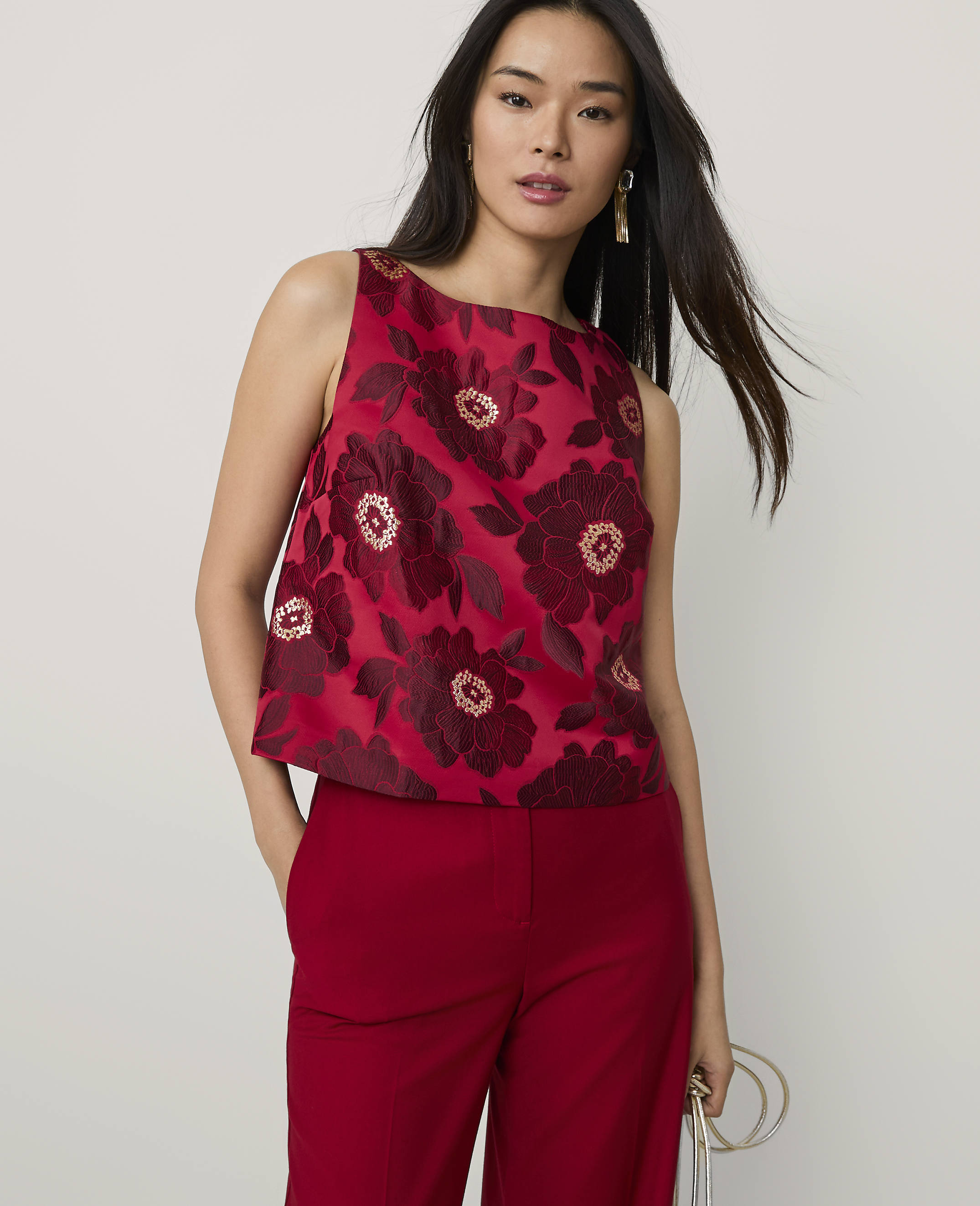 A woman wearing a red floral sleeveless top and matching red trousers stands against a plain light grey background.