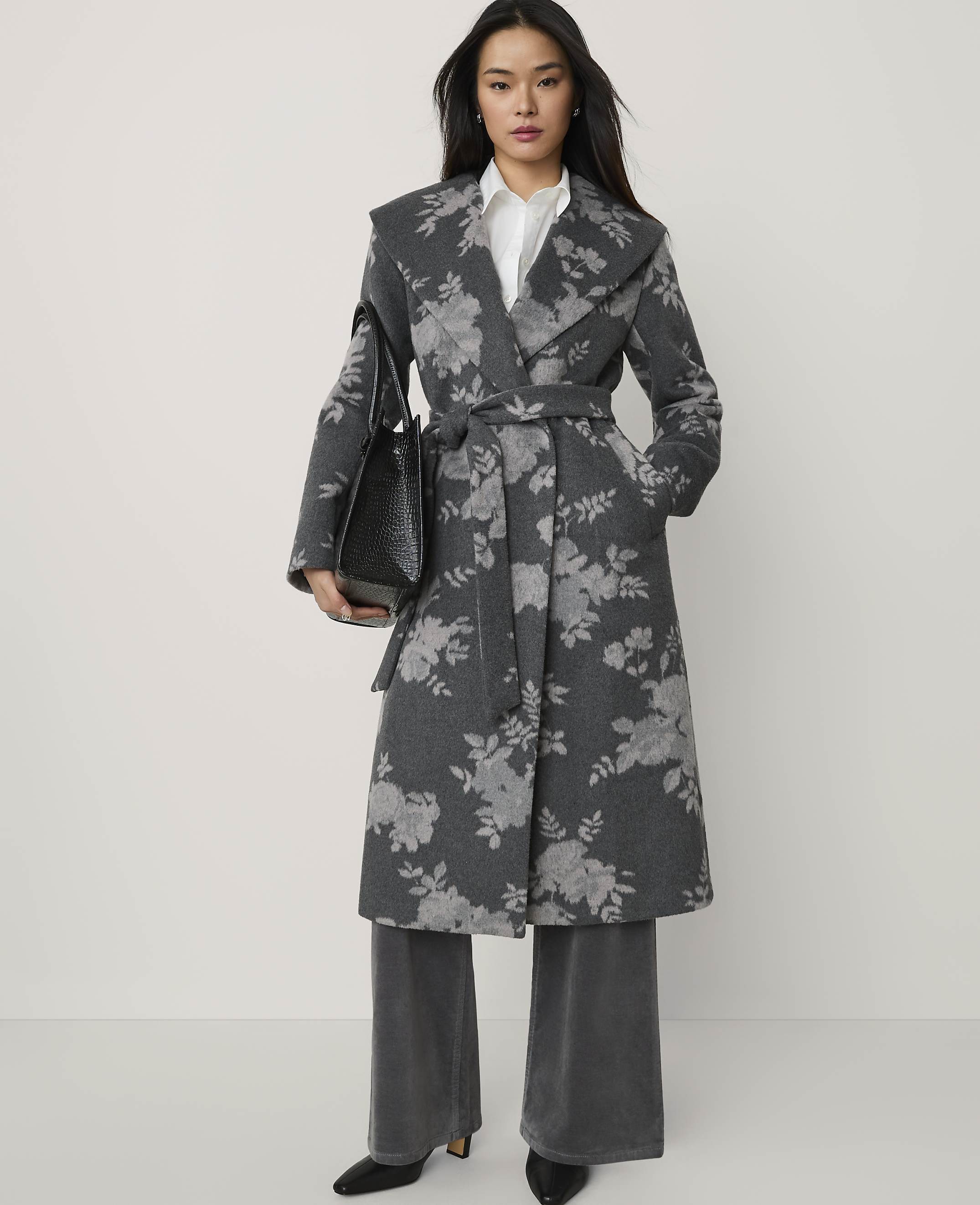 A woman wearing a grey floral-patterned wrap coat and wide-leg trousers stands against a plain white background.