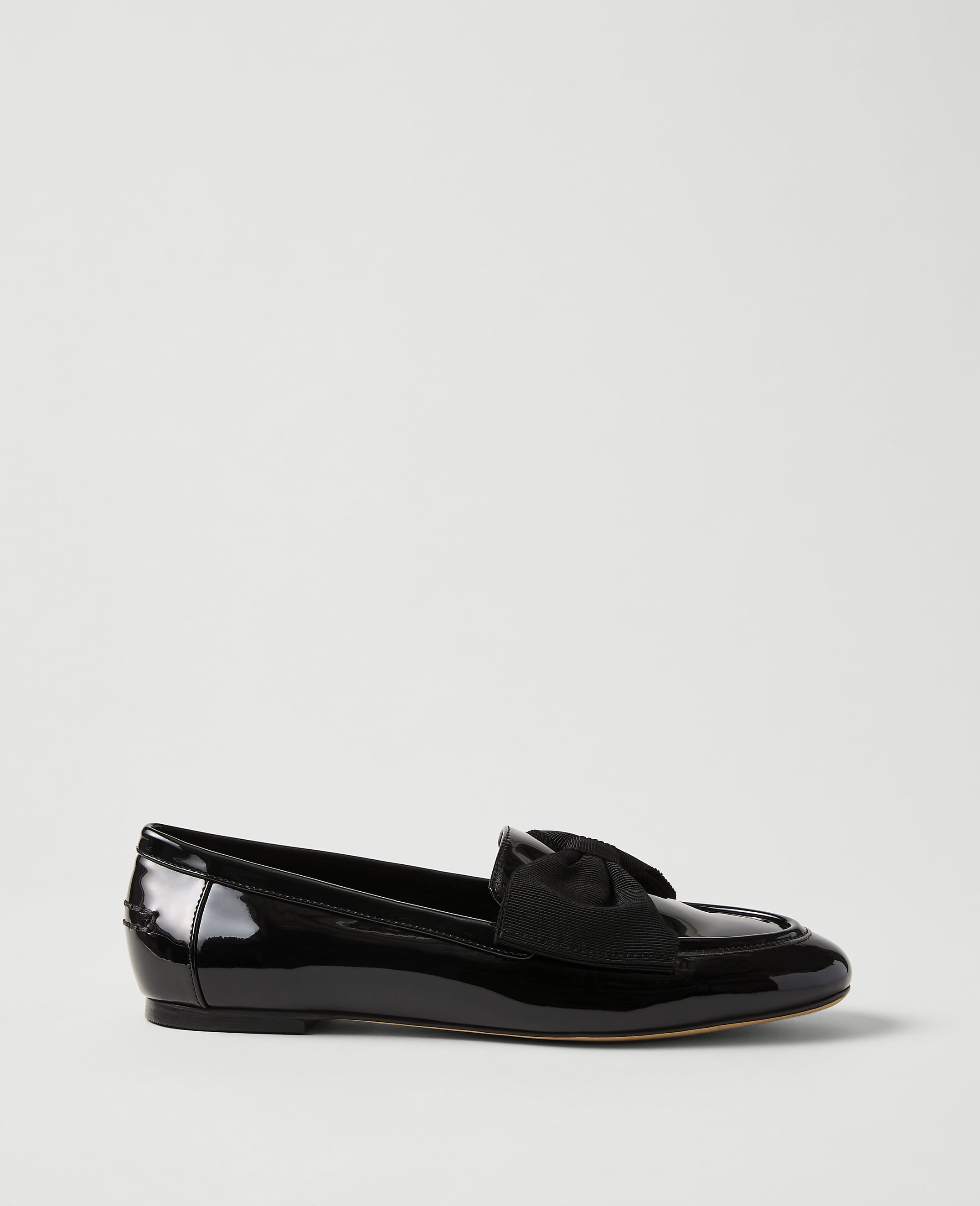 A single black patent leather loafer with a bow detail sits against a plain, light grey background.