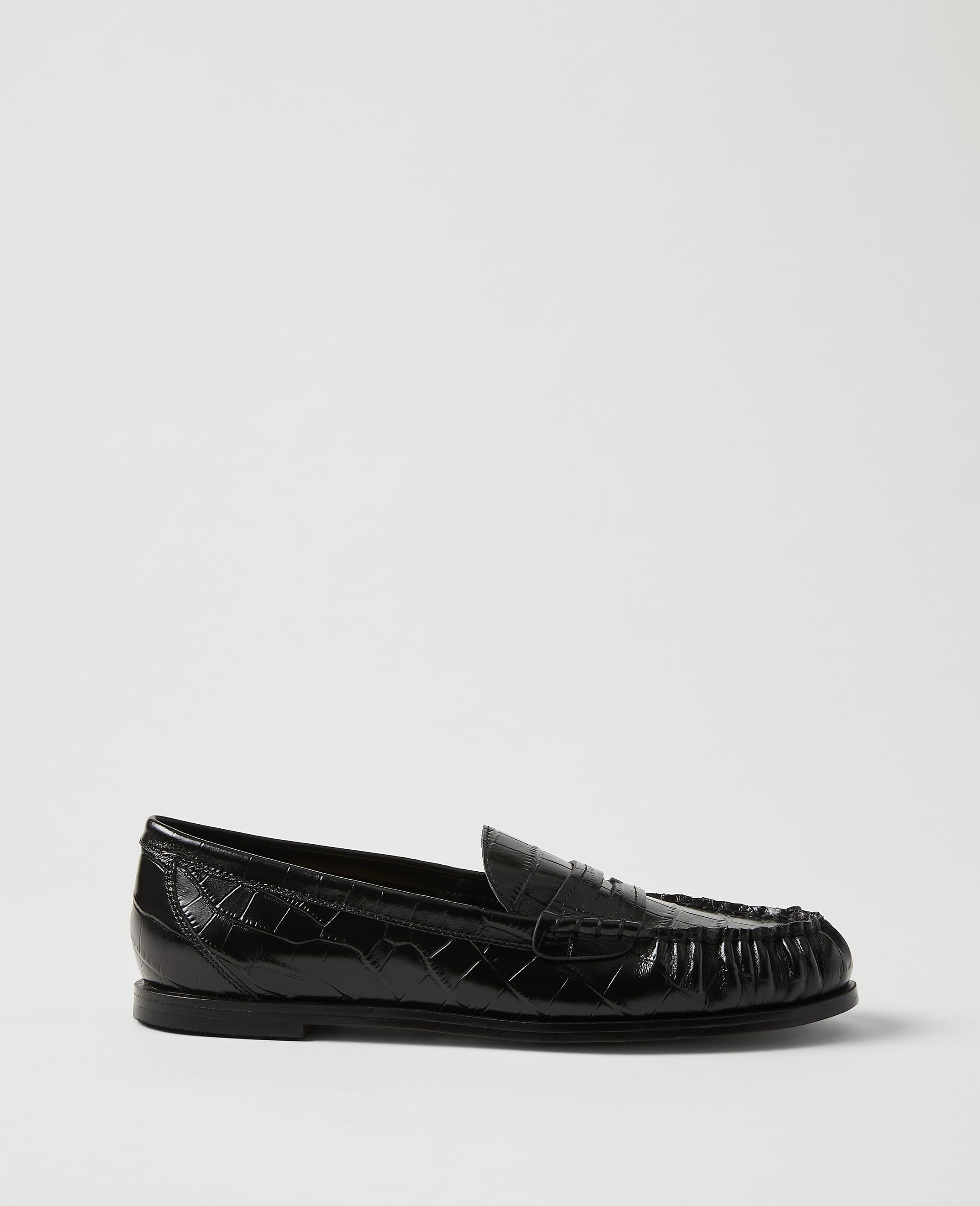 A single black crocodile-embossed leather loafer sits in the foreground against a plain, light grey background.