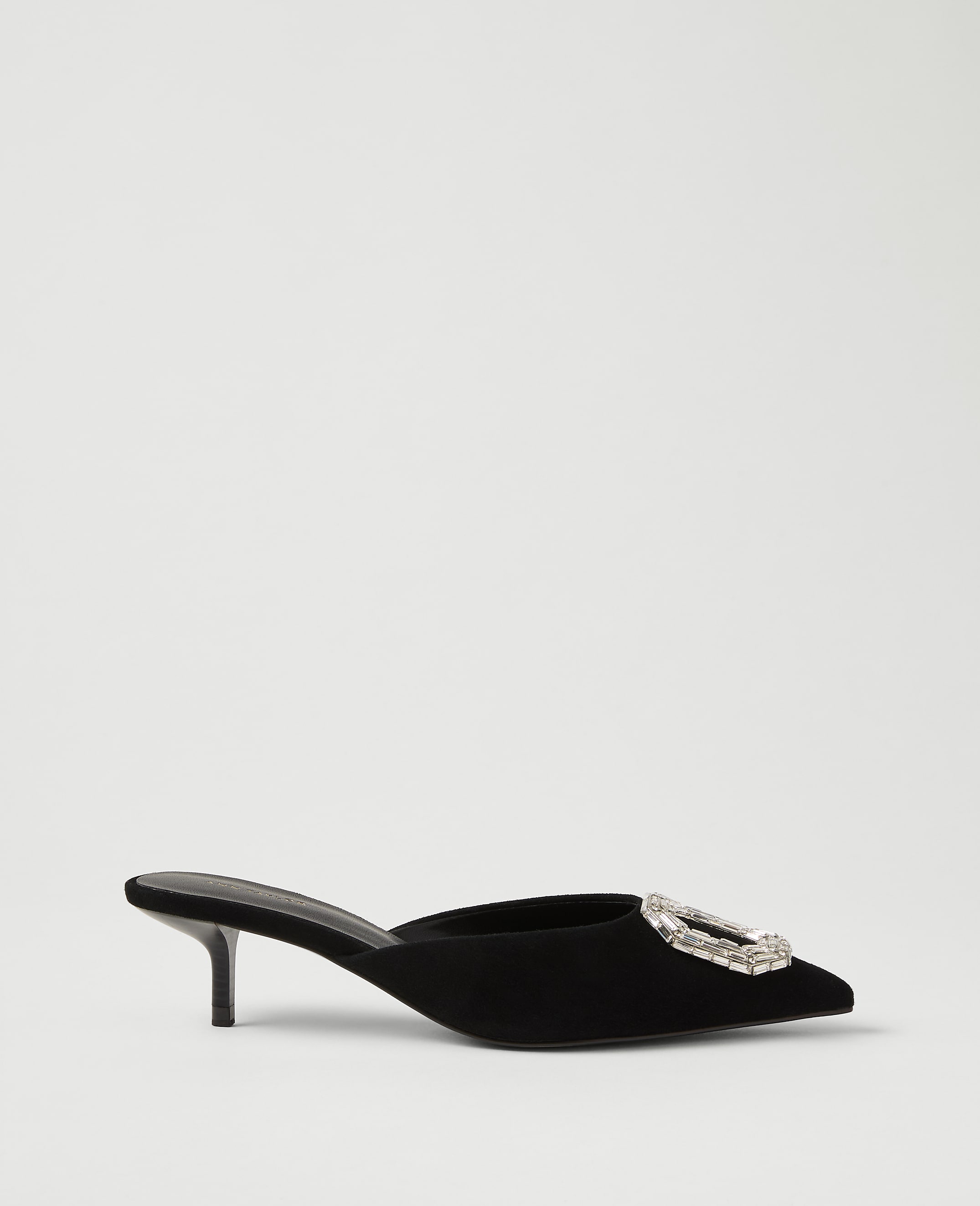 A black velvet pointed-toe mule with a crystal buckle sits against a plain light gray background.