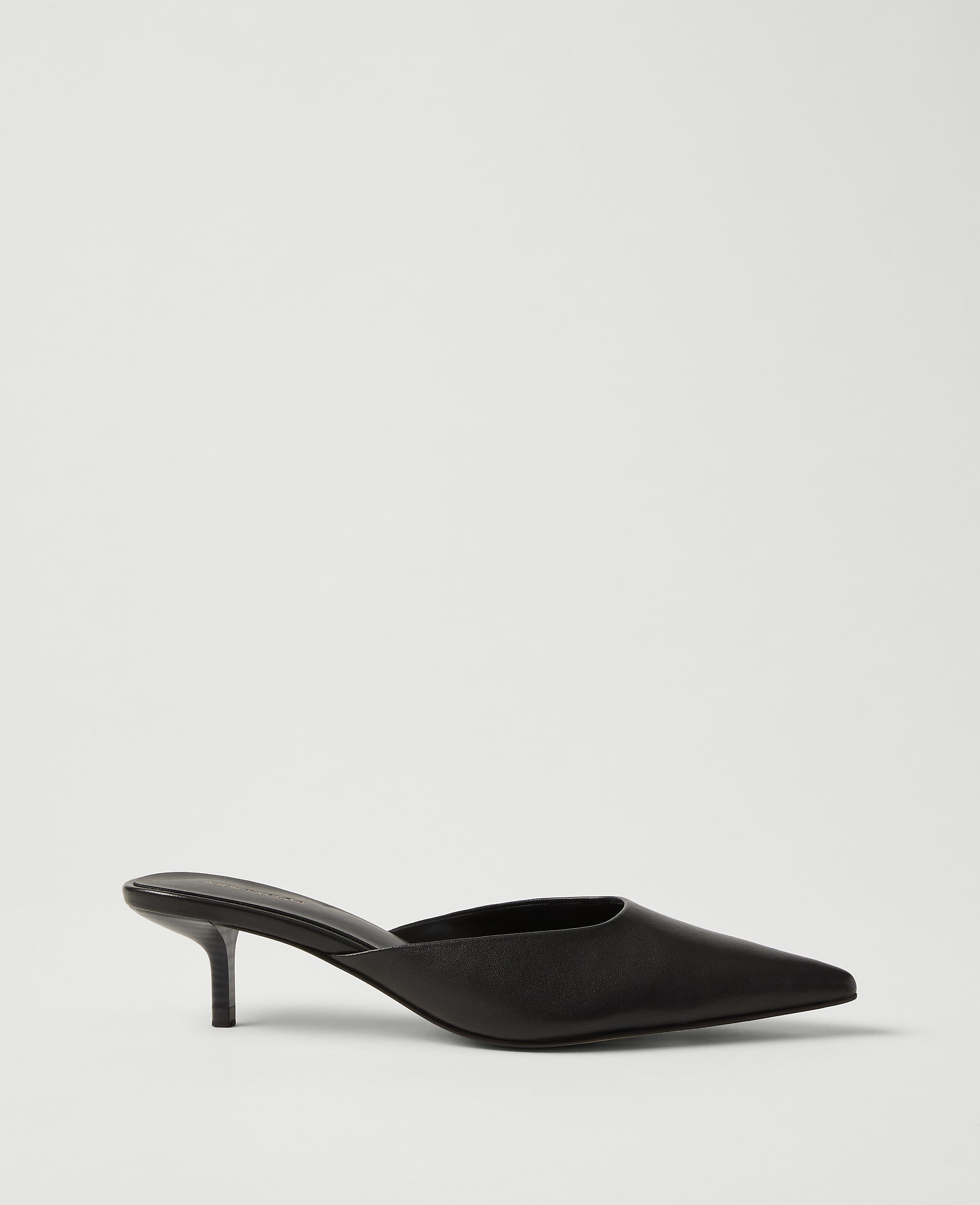 A single black pointed-toe kitten heel mule sits in the foreground against a plain, light gray background.
