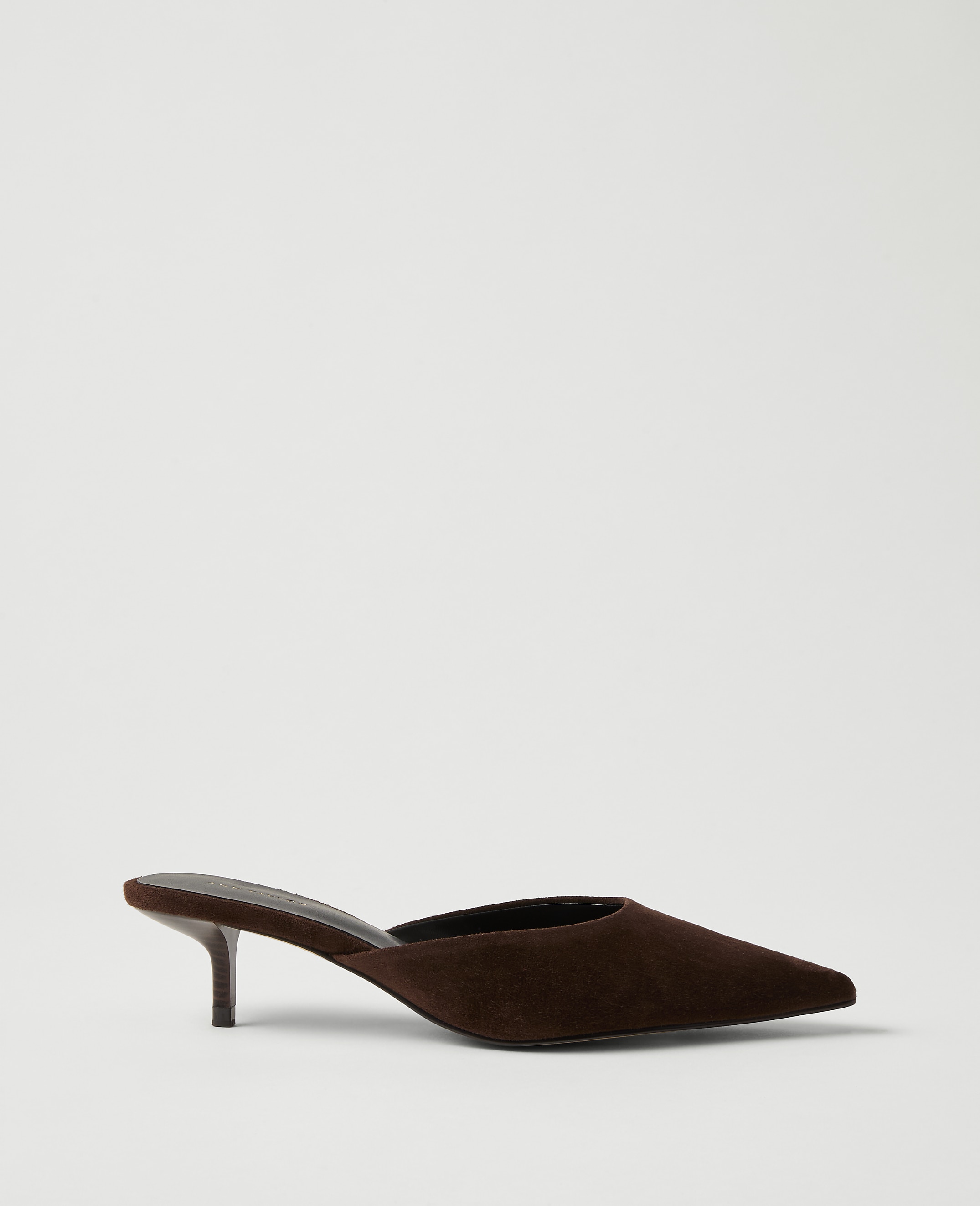 A brown suede pointed-toe mule heel sits against a plain, light gray background.