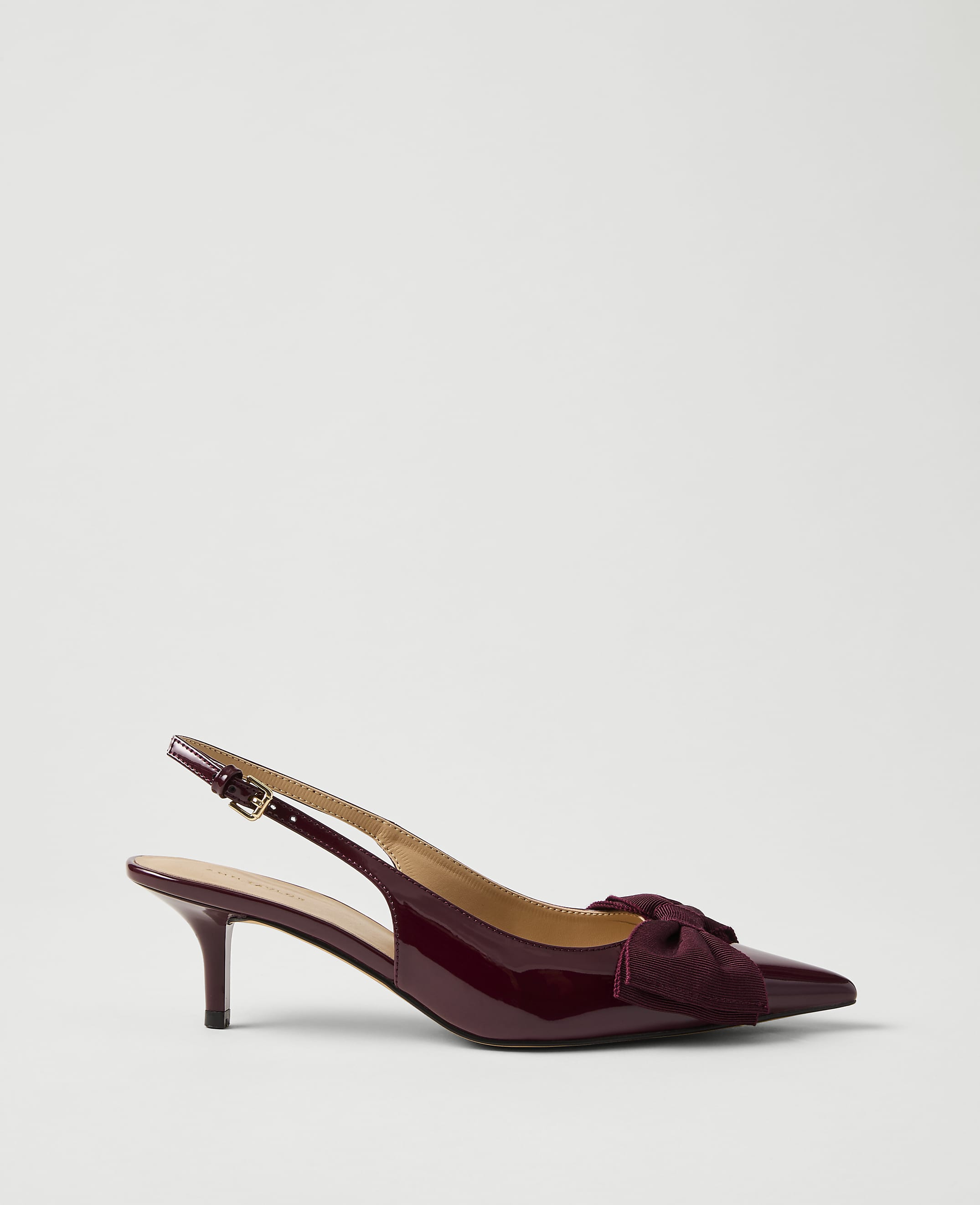 A single burgundy patent leather slingback heel with a bow sits against a plain, light grey background.
