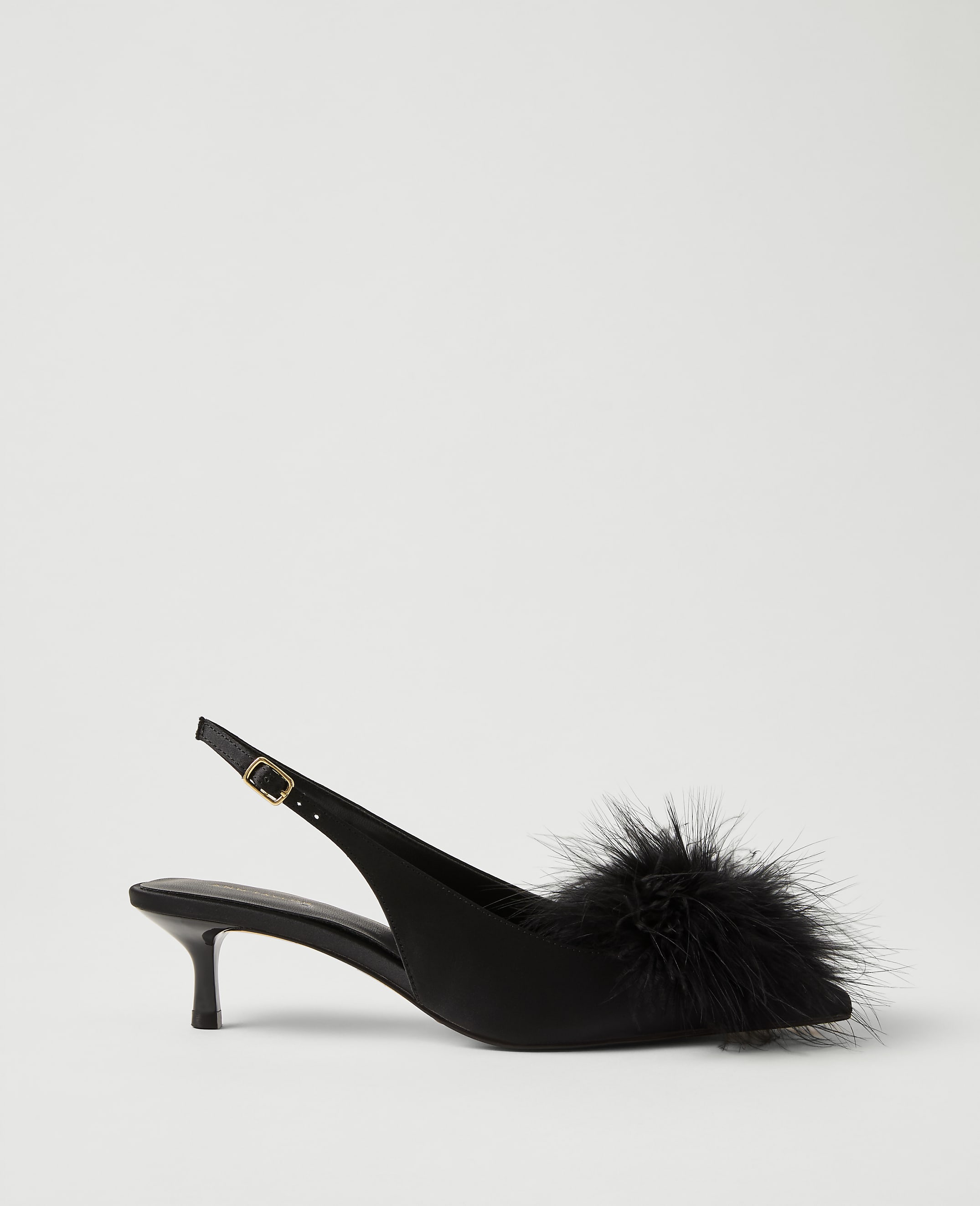 A black satin slingback heel with a fluffy feather pompom on the toe sits against a plain light gray background.