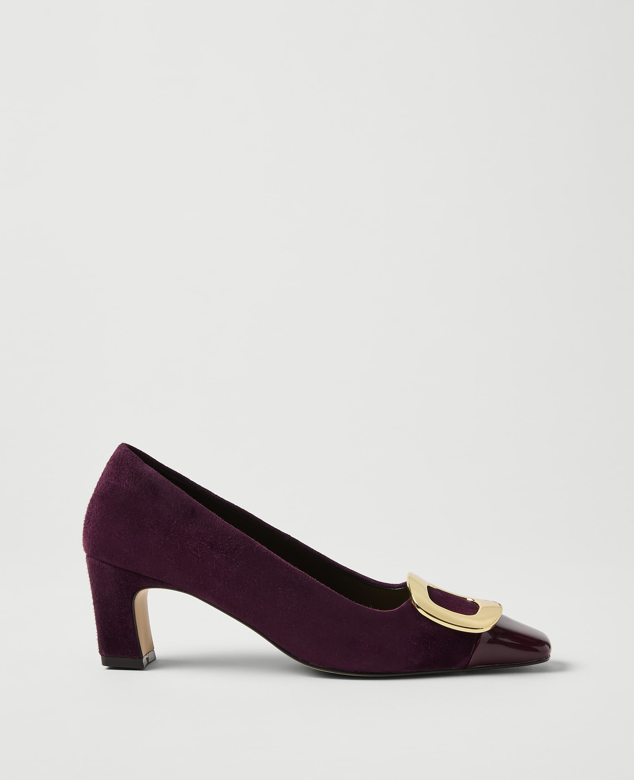 A purple velvet pump with a gold buckle and patent leather toe sits against a plain light gray background.