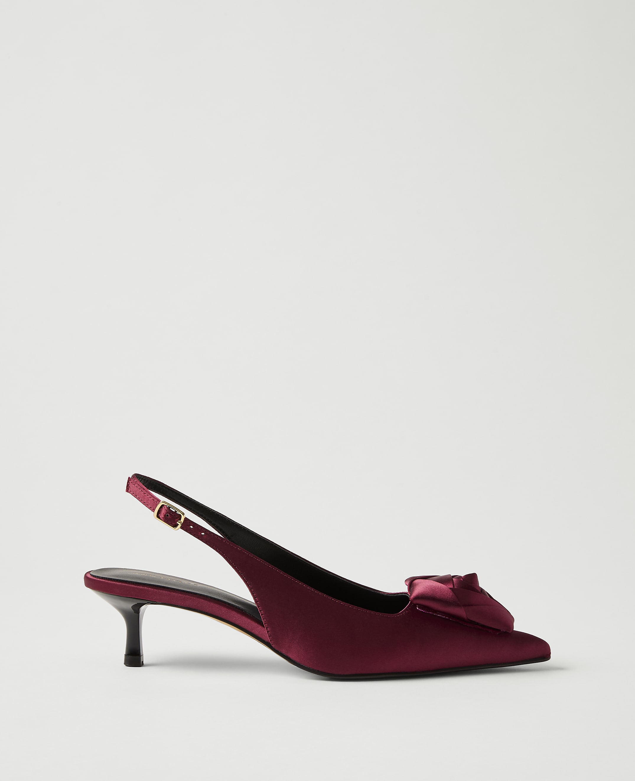 A deep red satin slingback heel with a bow detail sits against a plain, light grey background.