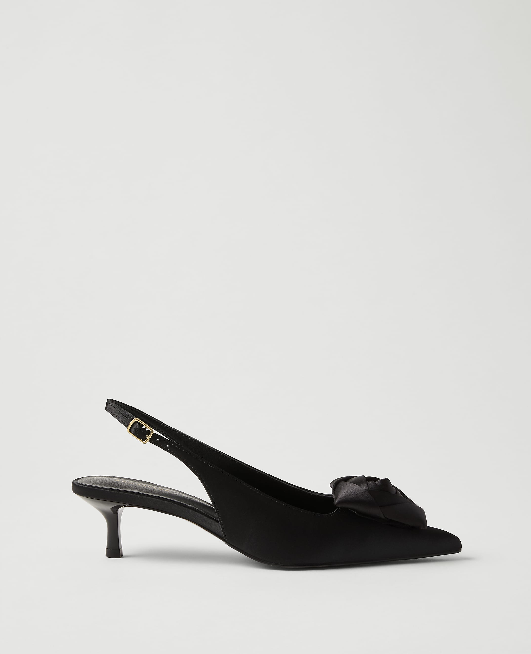 A black satin slingback heel with a decorative bow sits in the foreground against a plain, light gray background.