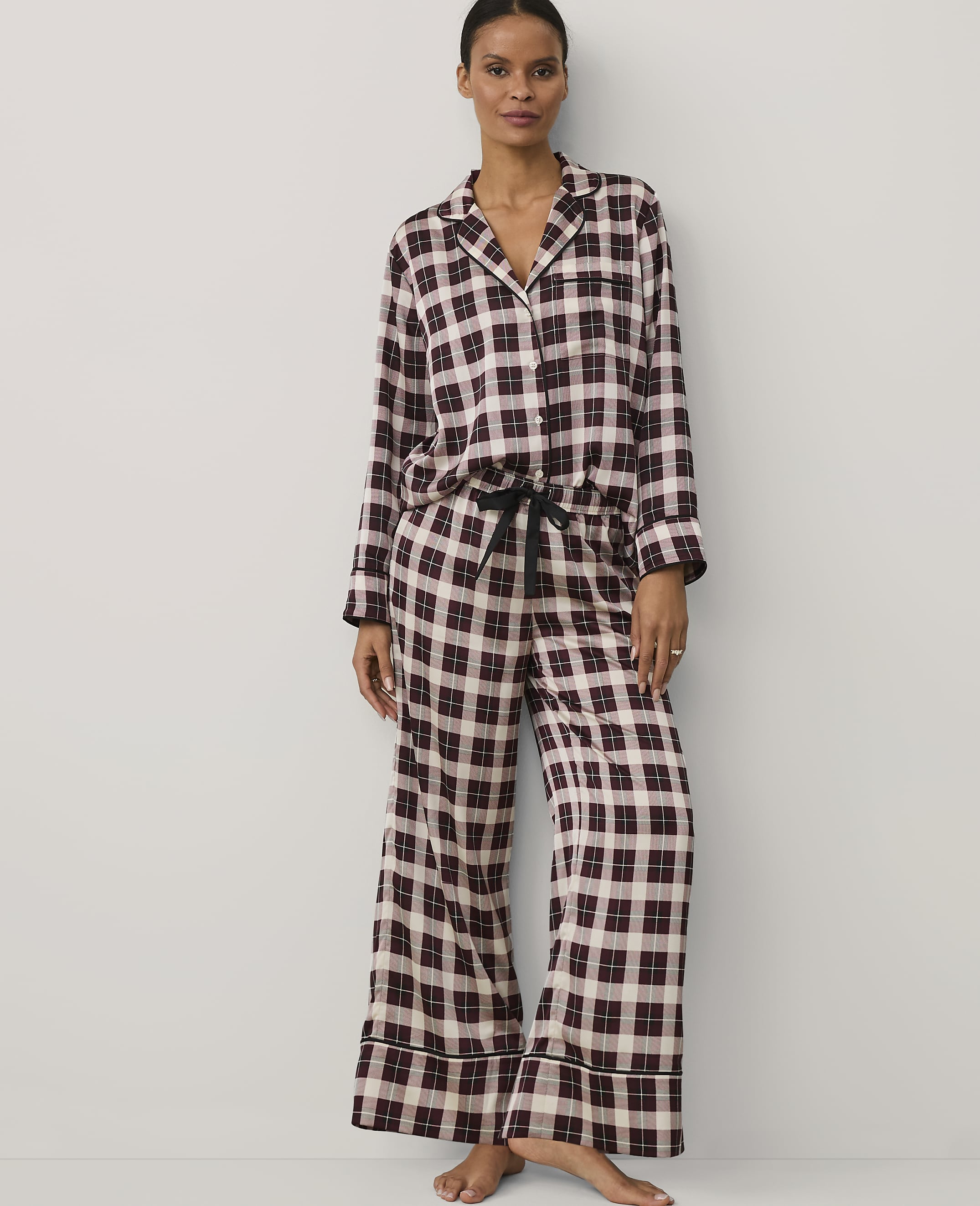 A woman wearing burgundy and white checkered pajamas stands against a plain white background.
