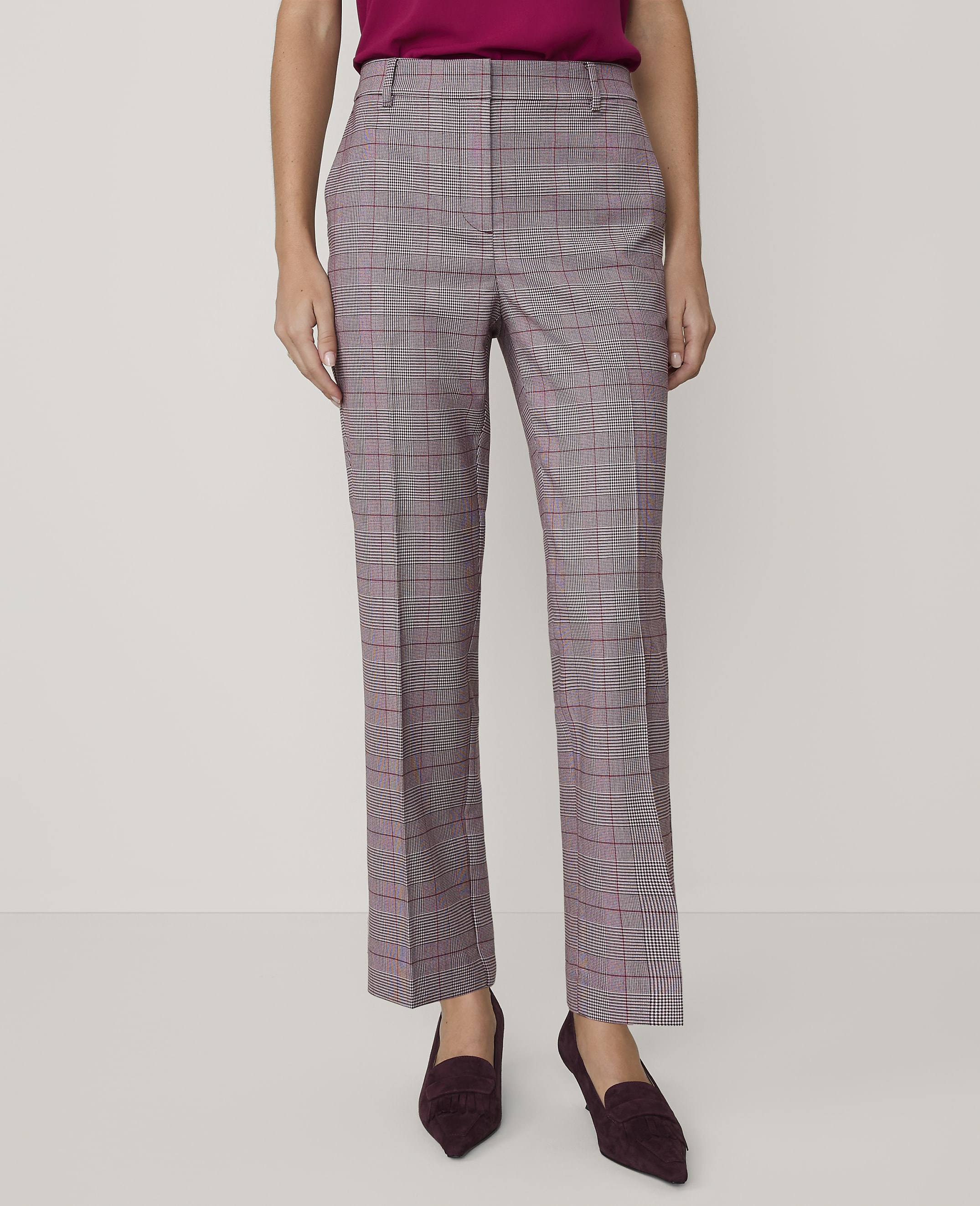 A person wearing a magenta top, plaid trousers, and dark purple heels stands against a plain white background.