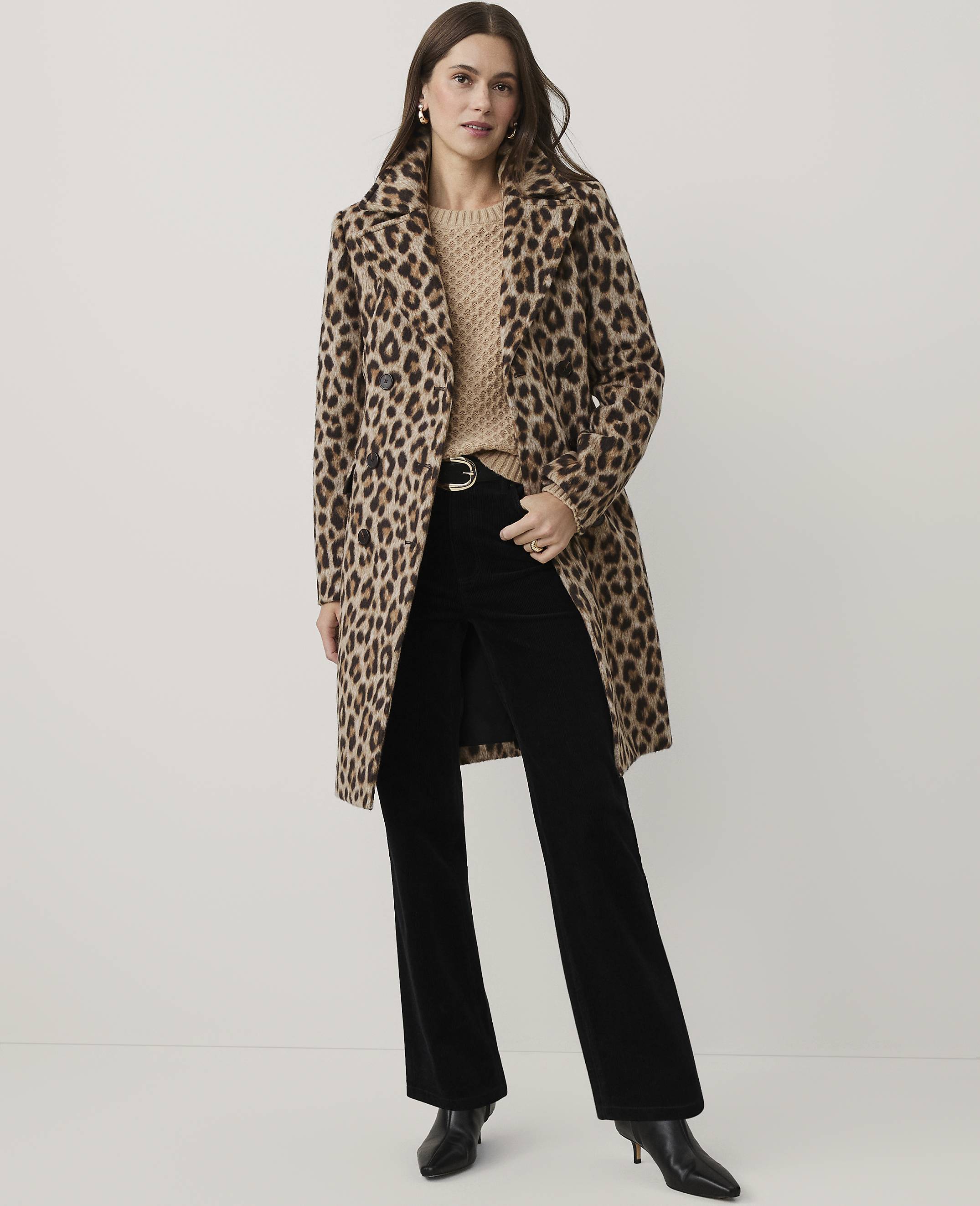 A woman wearing a leopard print coat, beige sweater, and black flared trousers stands against a plain white background.