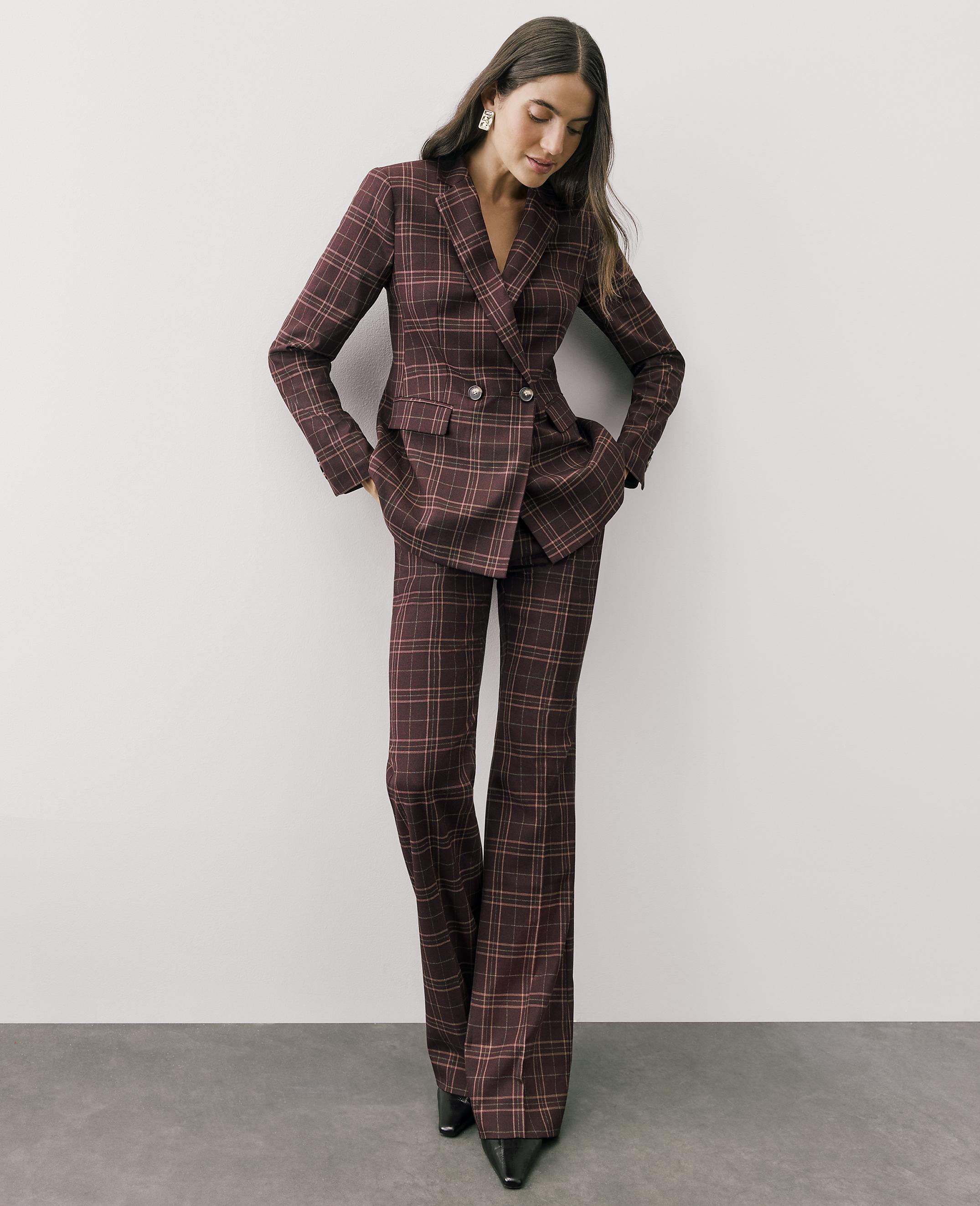 A woman wearing a burgundy plaid pantsuit stands against a plain white wall and grey floor.