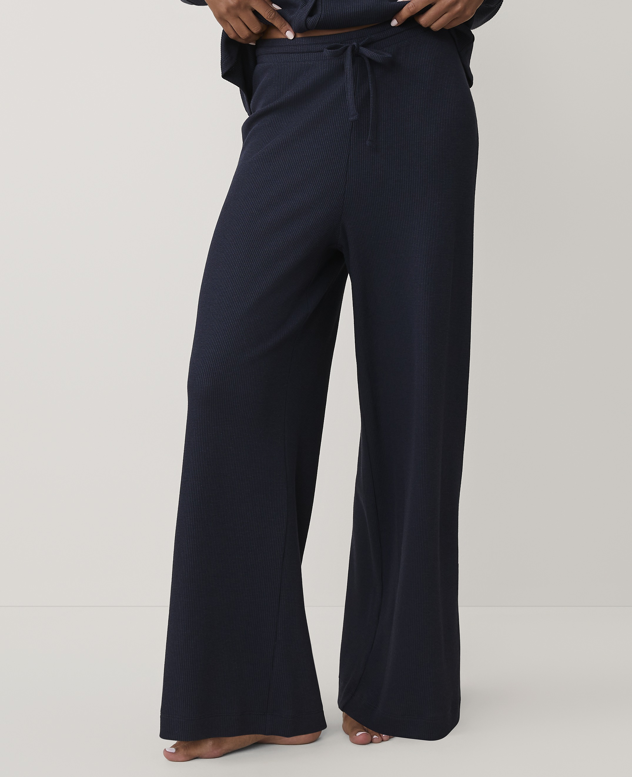 A person wears navy blue wide-leg ribbed trousers against a plain, light-colored background.