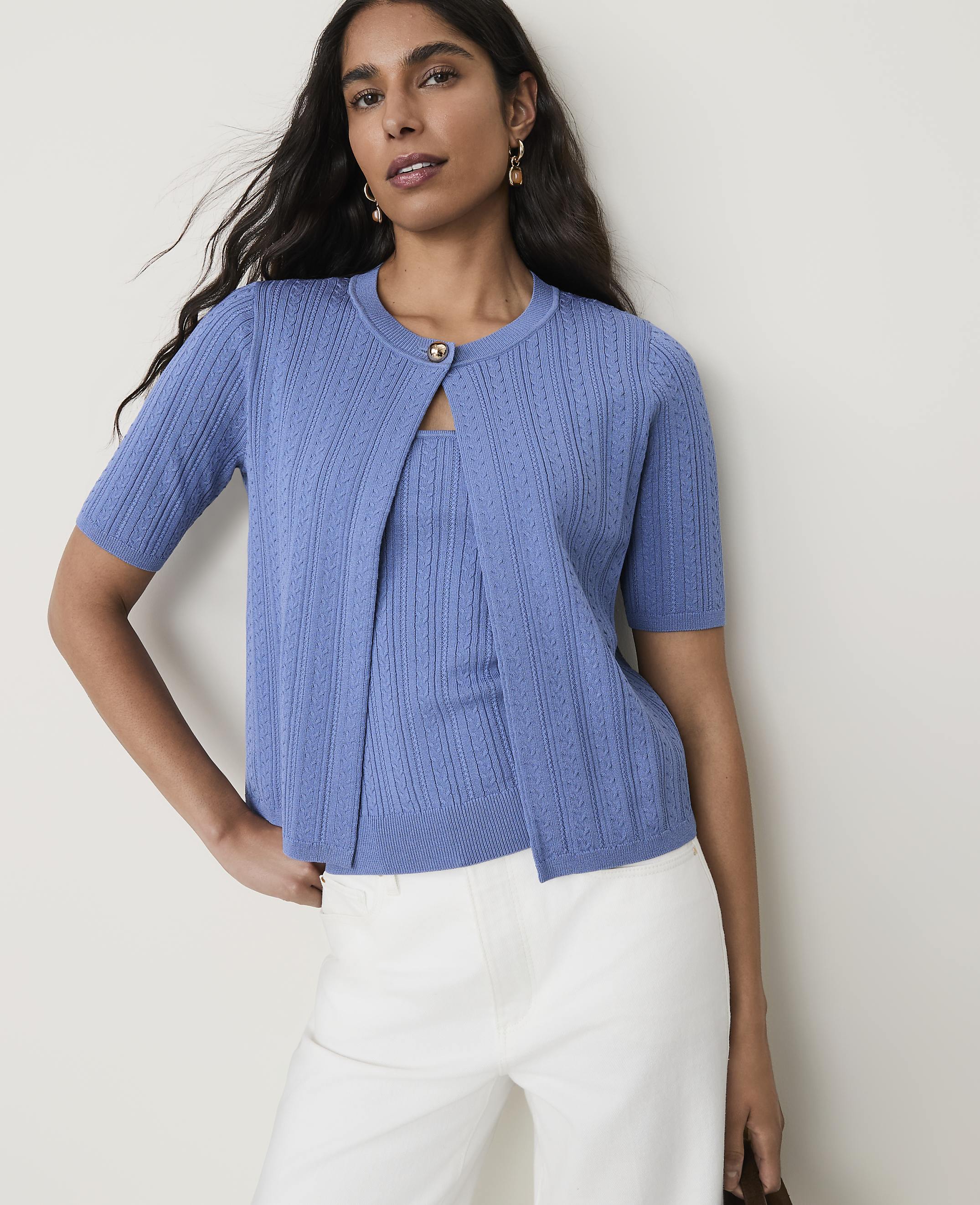 A woman in a blue cardigan and matching top stands against a plain, light-colored background.