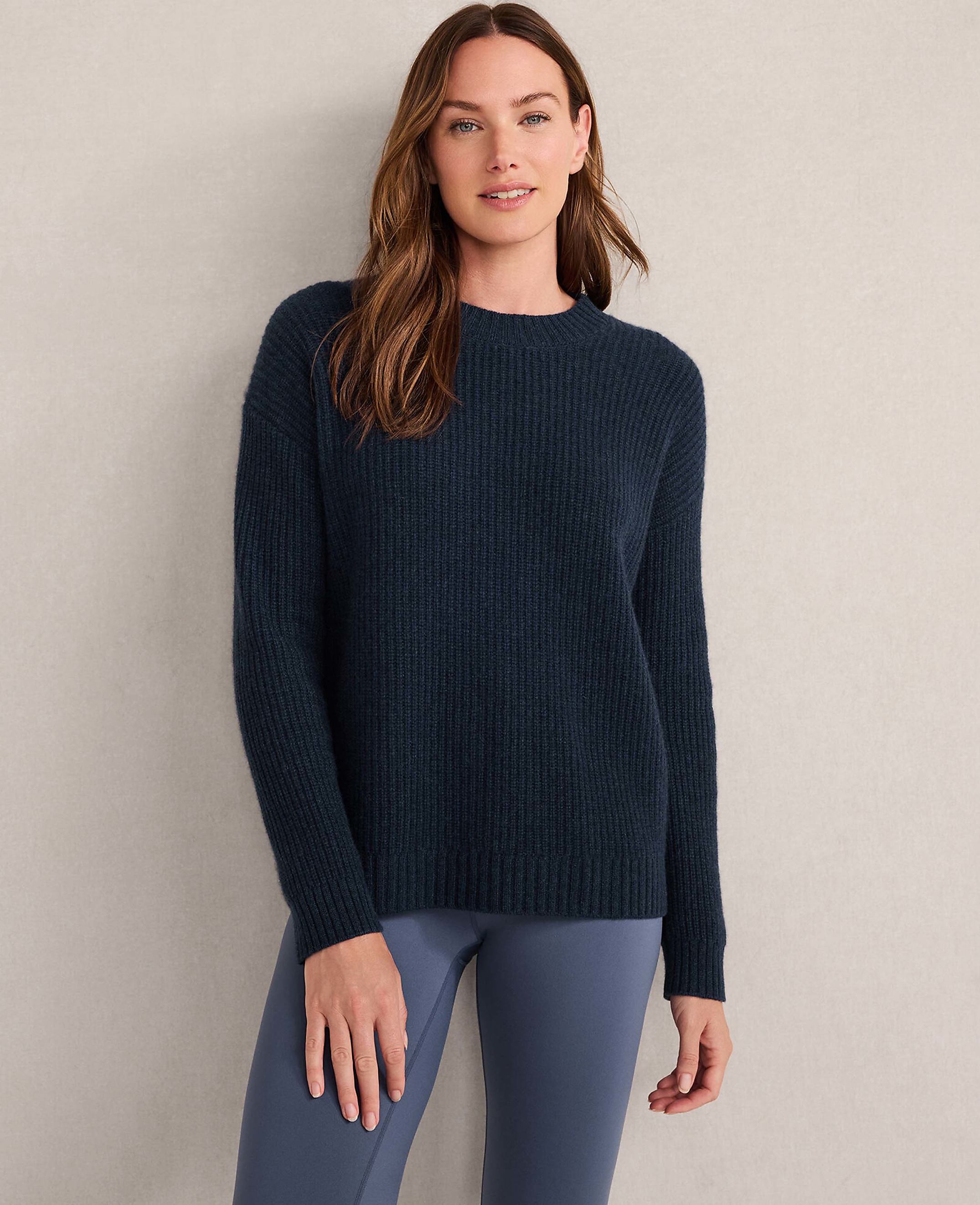A woman in a light gray ribbed sweater stands against a textured, neutral background.