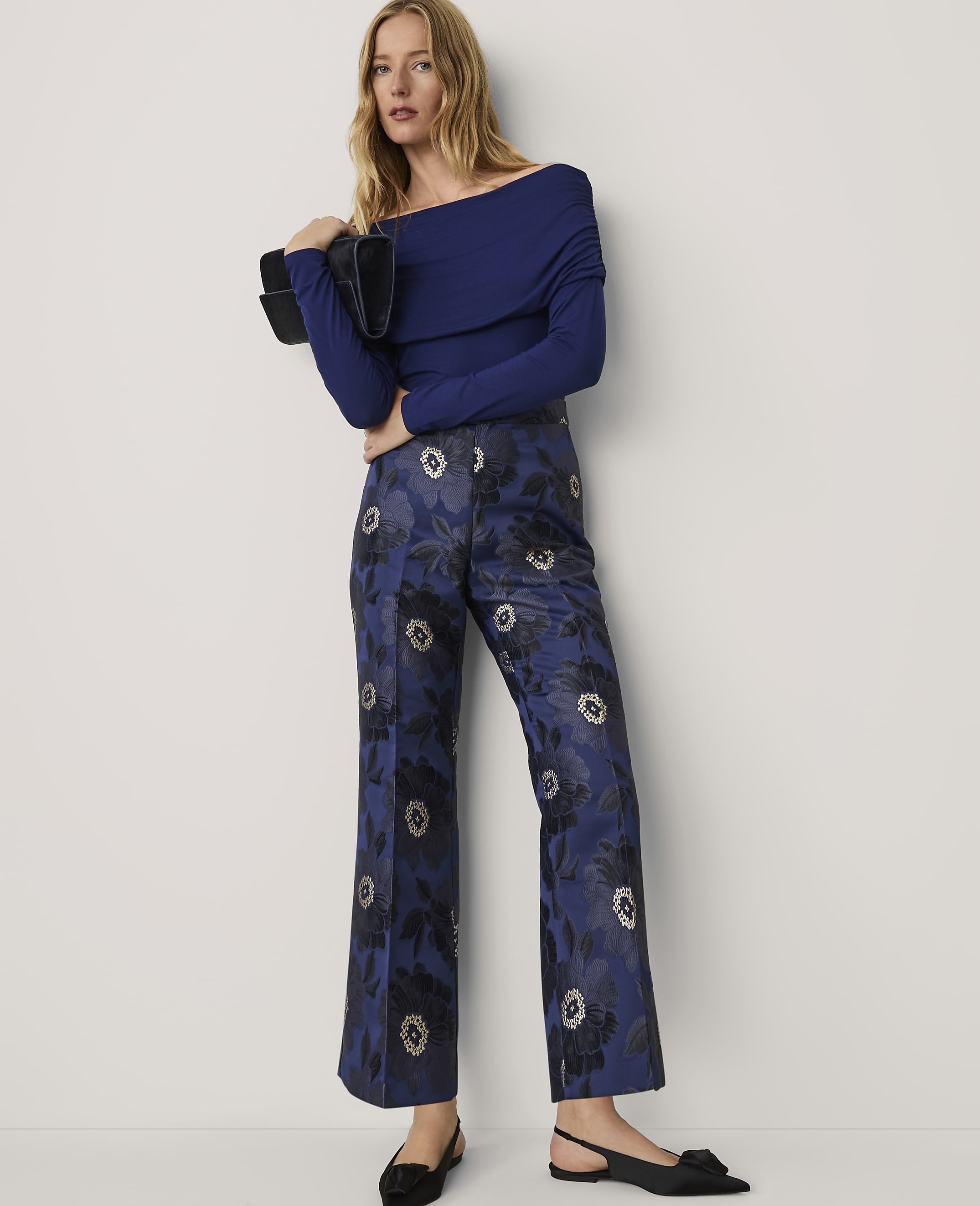 A woman wearing a blue off-the-shoulder top and floral patterned blue trousers stands against a plain white background.