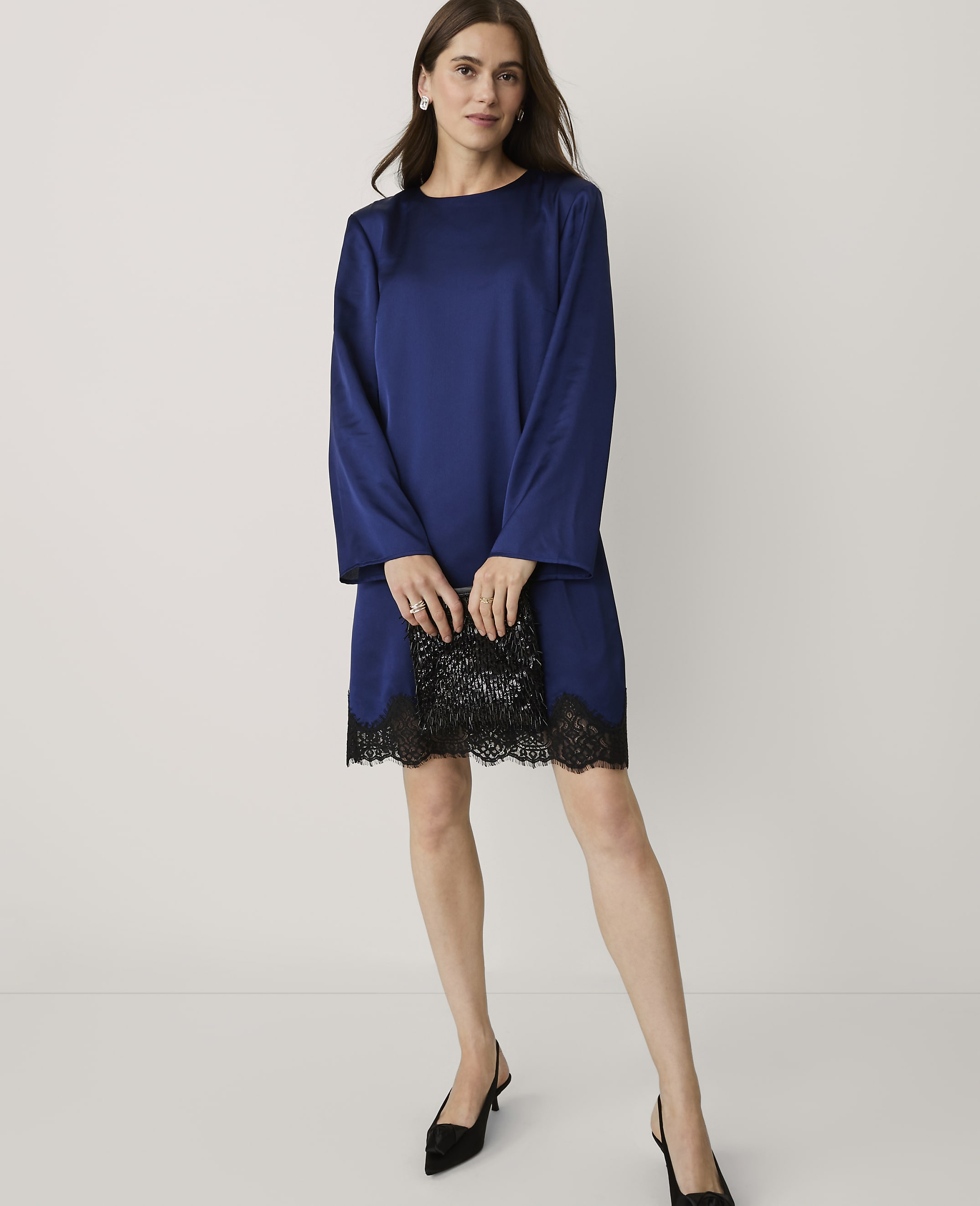 A woman wearing a royal blue satin dress with black lace trim and black heels stands against a plain white background.