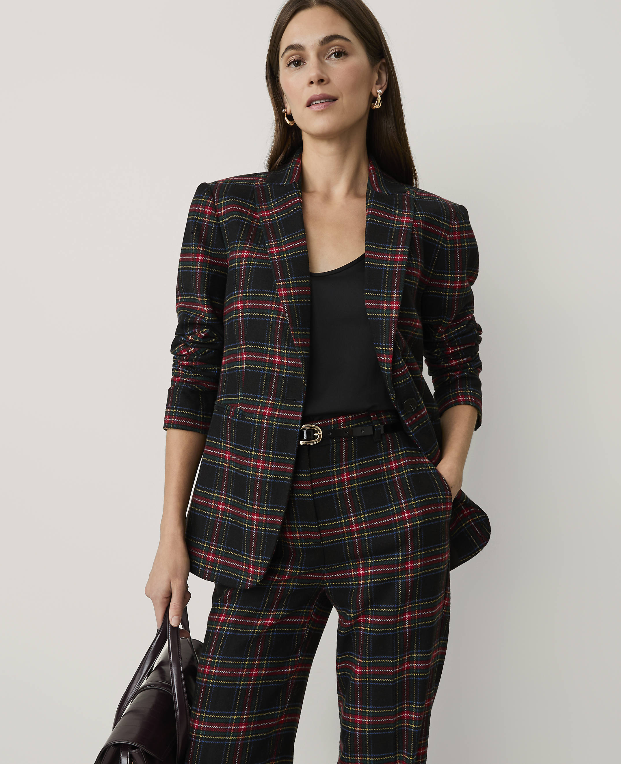 A woman wearing a red and black plaid suit stands against a plain, light-colored background.