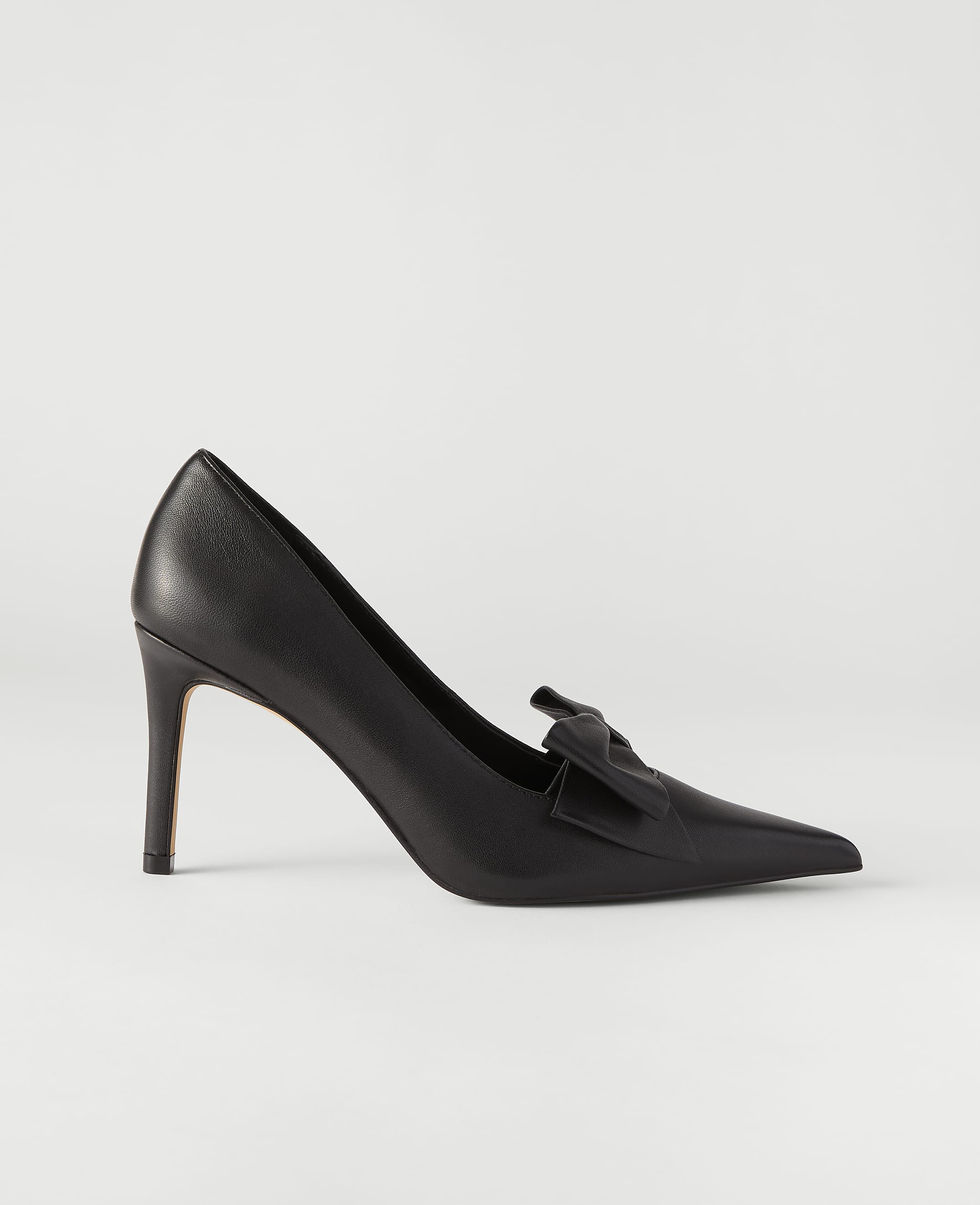 A single black pointed-toe pump with a bow detail sits in the foreground against a plain, light gray background.
